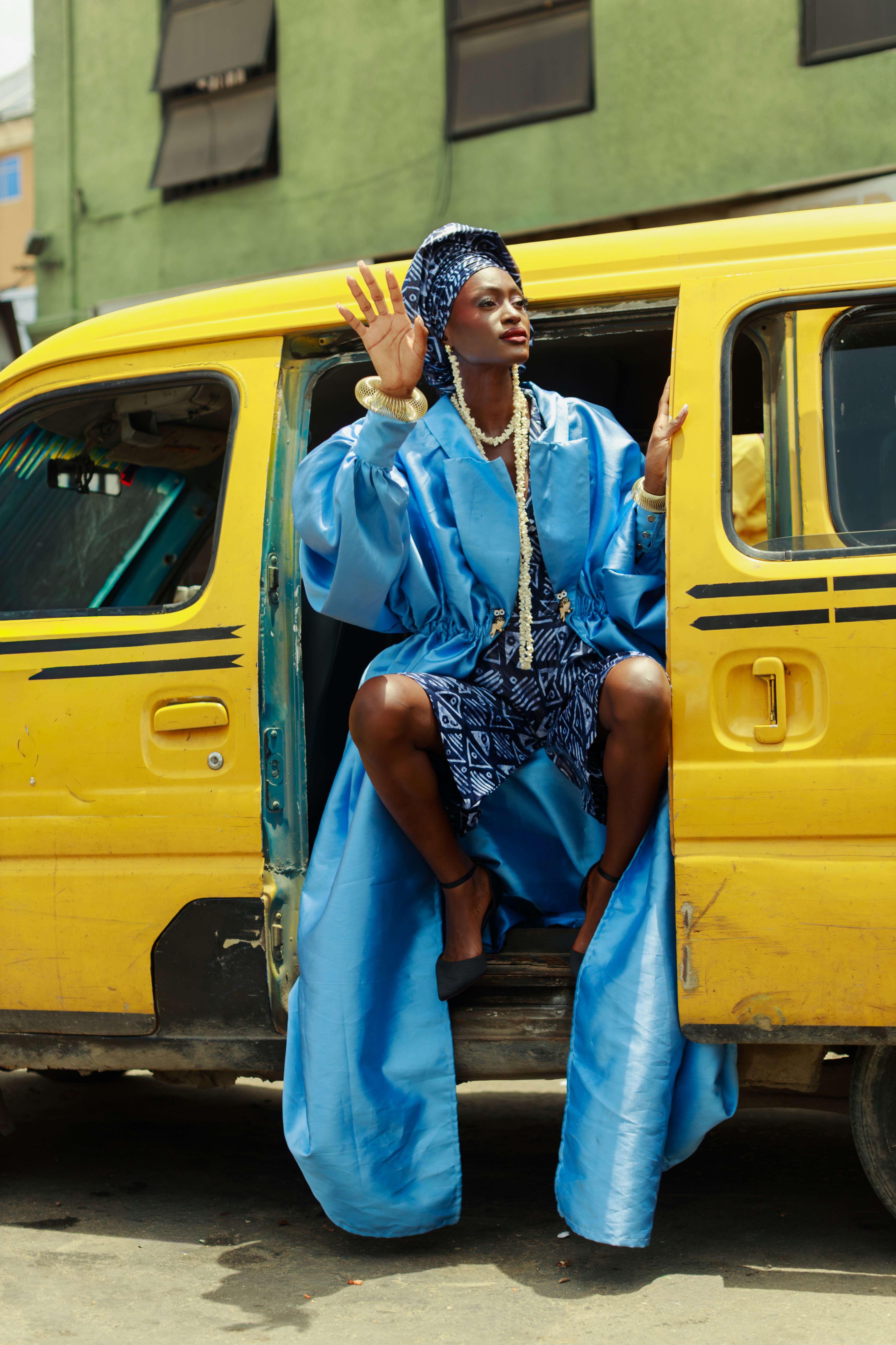 A woman in a blue coat and headwrap sitting in a yellow van in Lagos