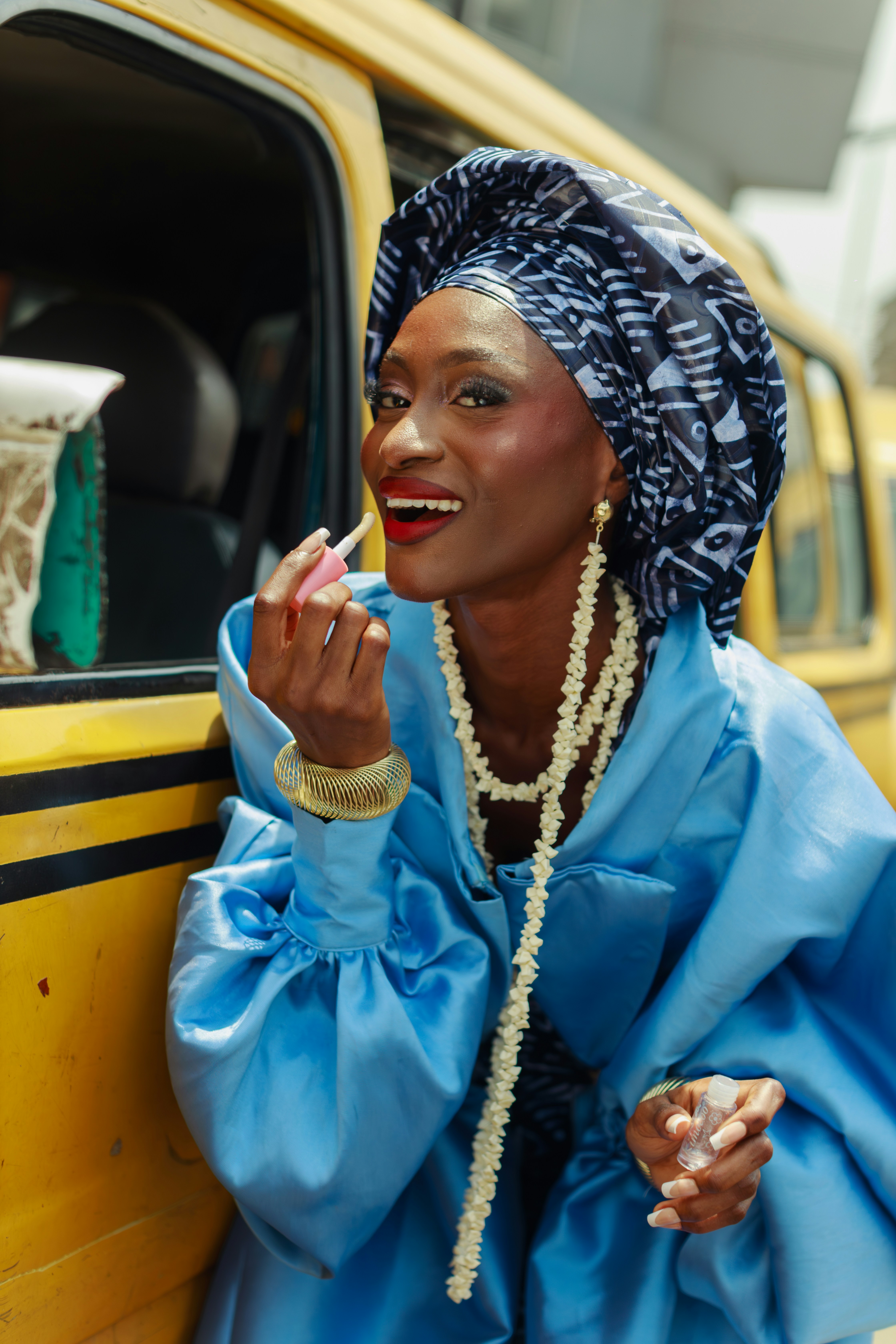 Uma mulher aplicando brilho labial ao lado de um veículo amarelo em Lagos, Nigéria