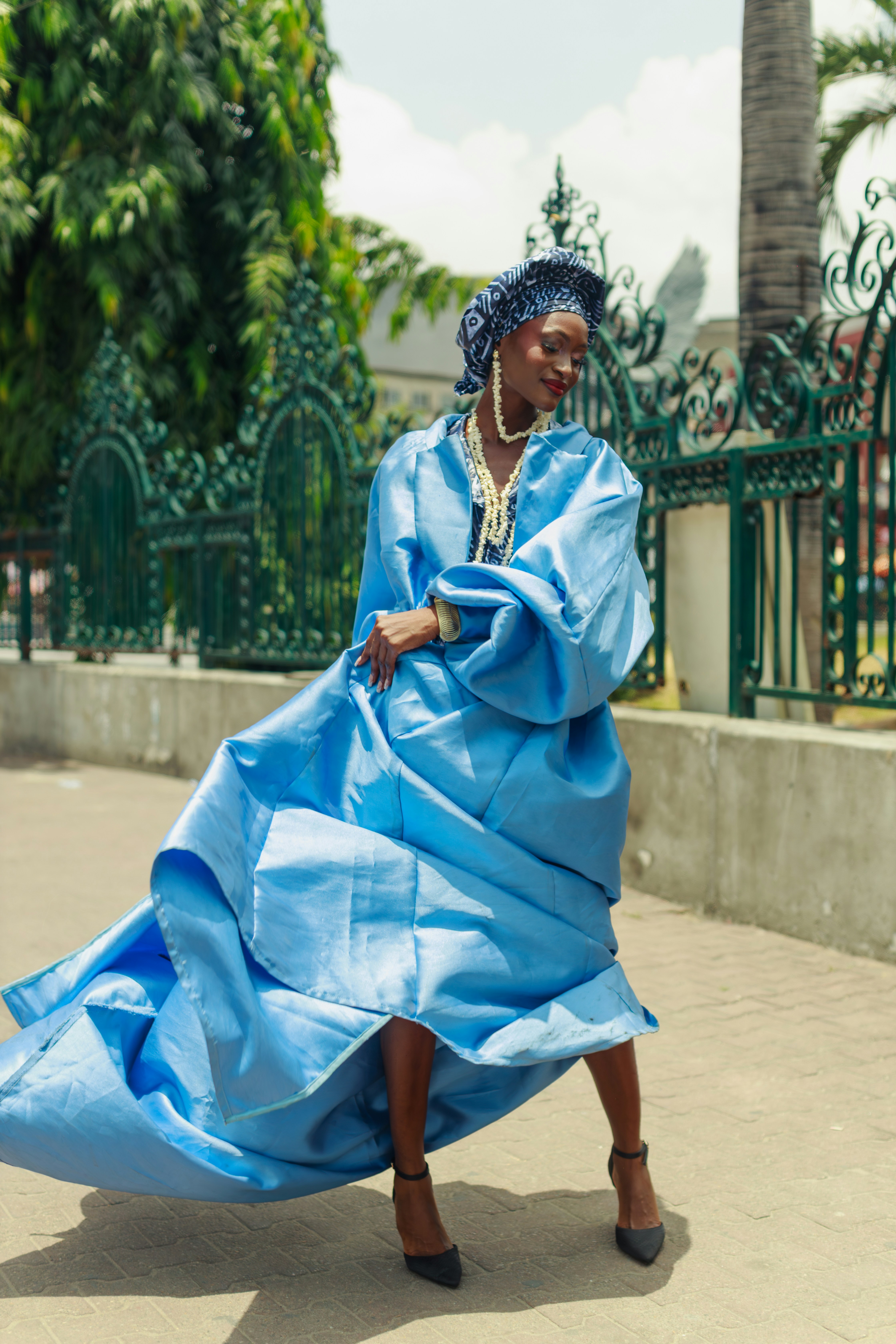 Uma mulher com um volumoso casaco de cetim azul e faixa de cabeça em uma rua de Lagos