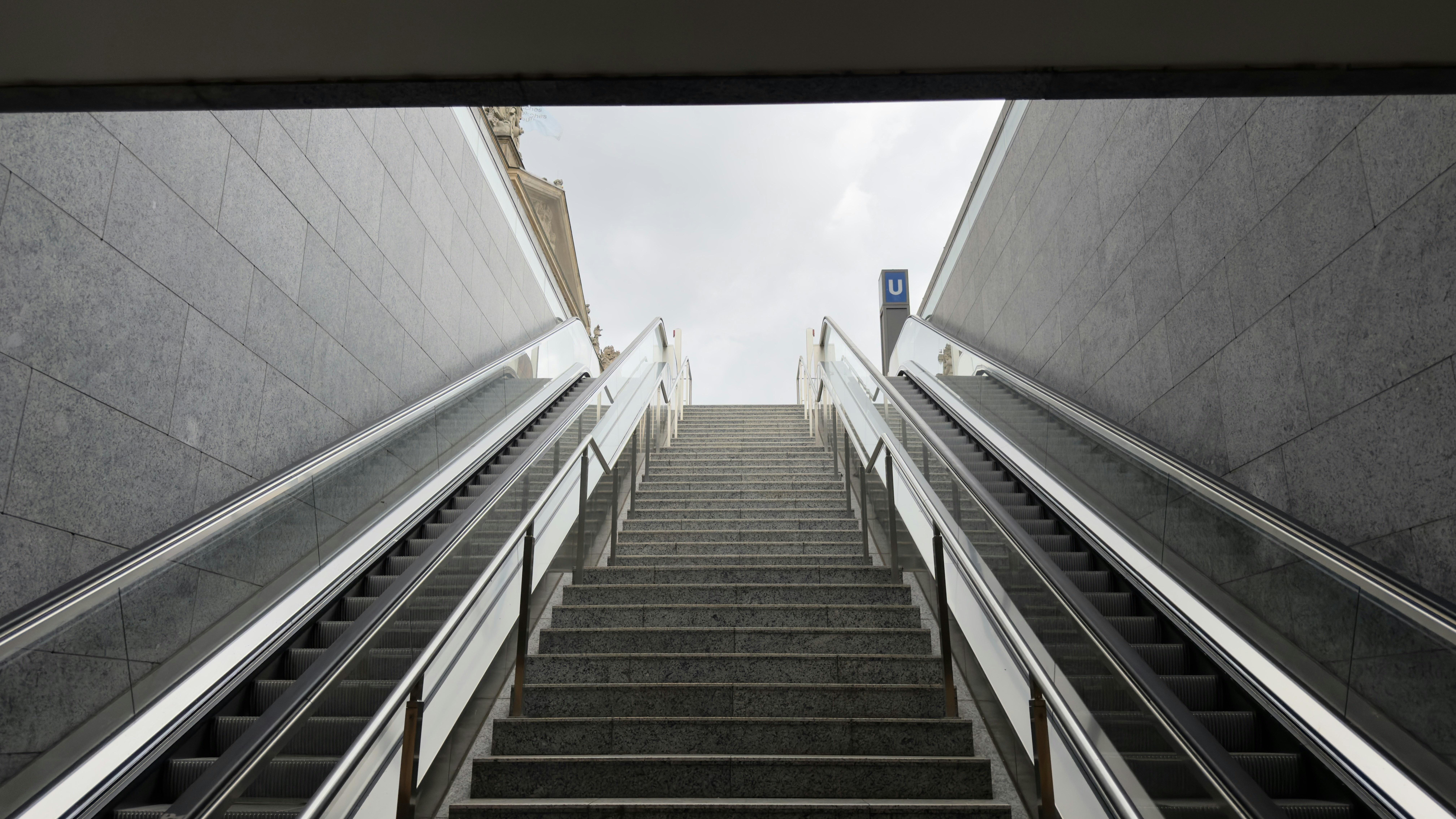 Stone stairs between two escalators leading up to a bright sky