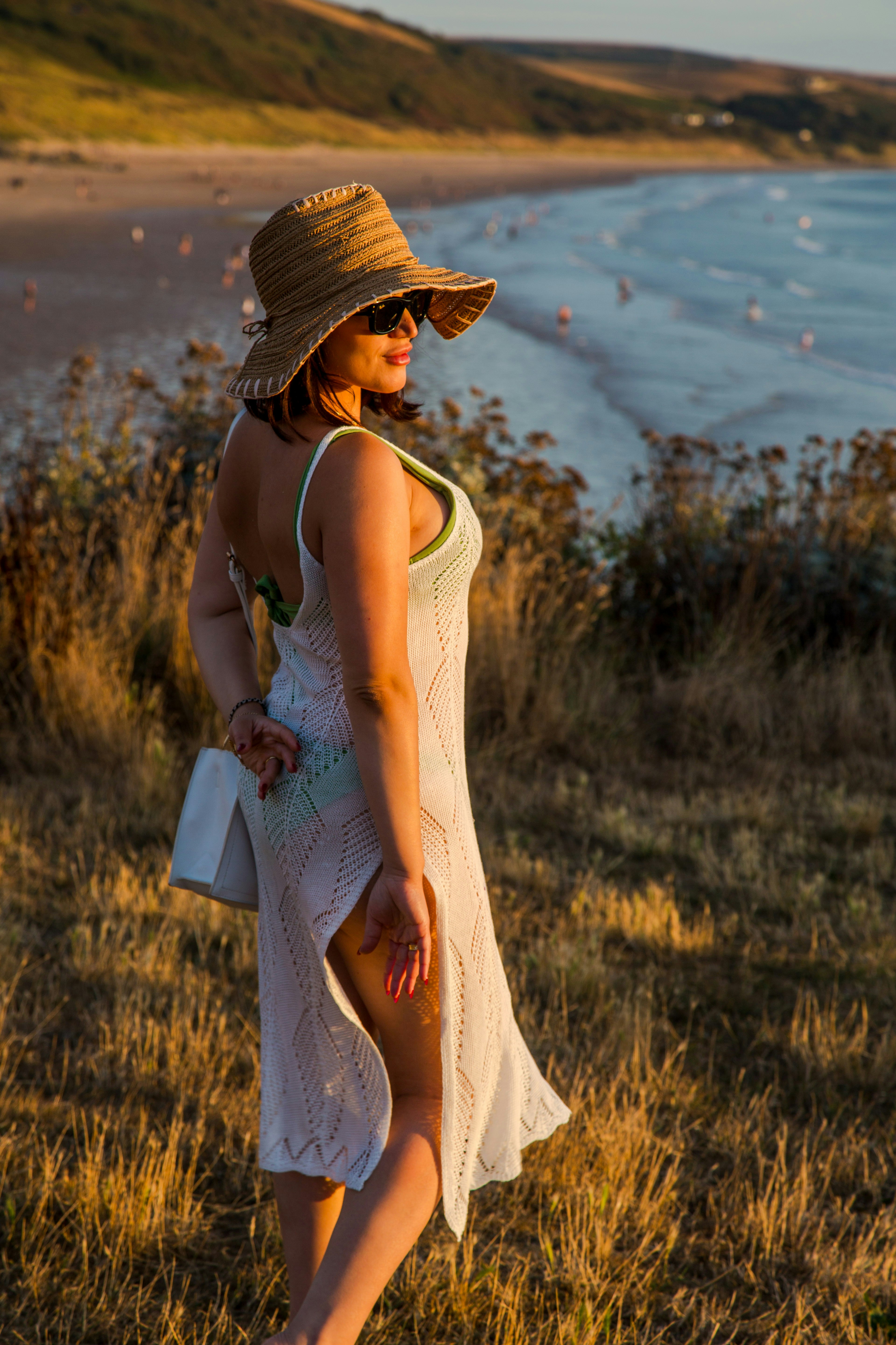 A woman in a white crochet dress and straw hat on a coastal cliff