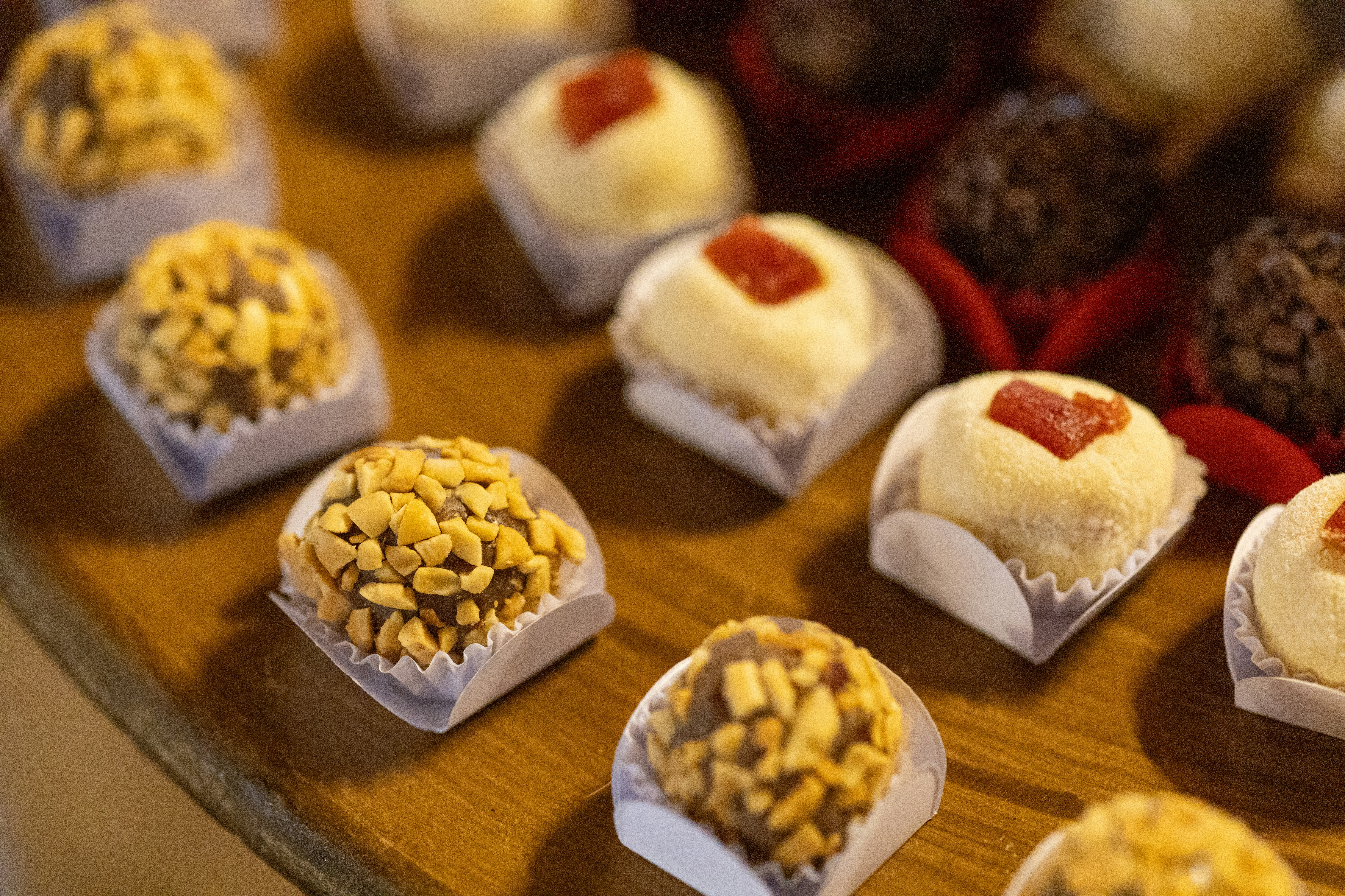 Assorted brigadeiro truffles with nut and fruit toppings on a wooden table