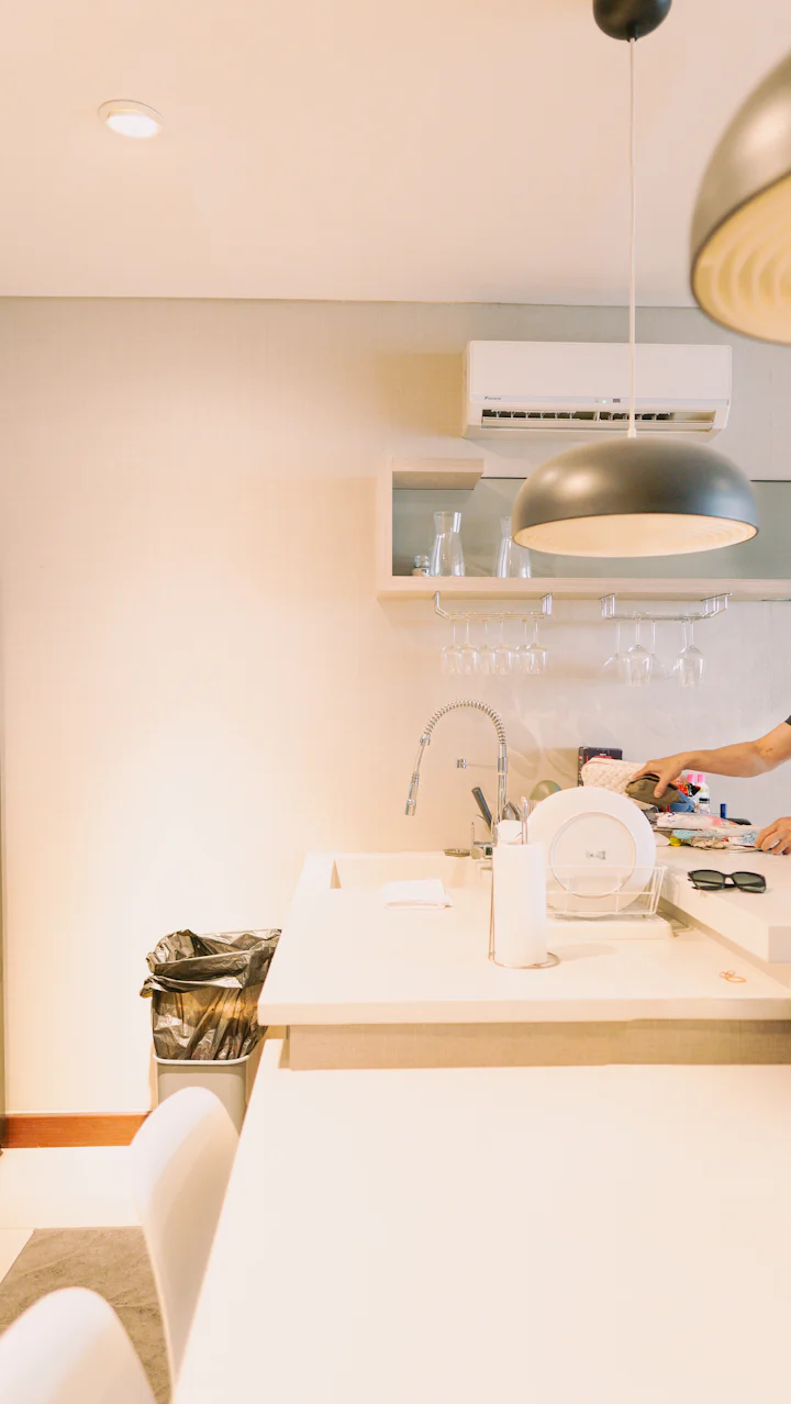 A person cleaning a kitchen counter with a white sink and hanging glasses