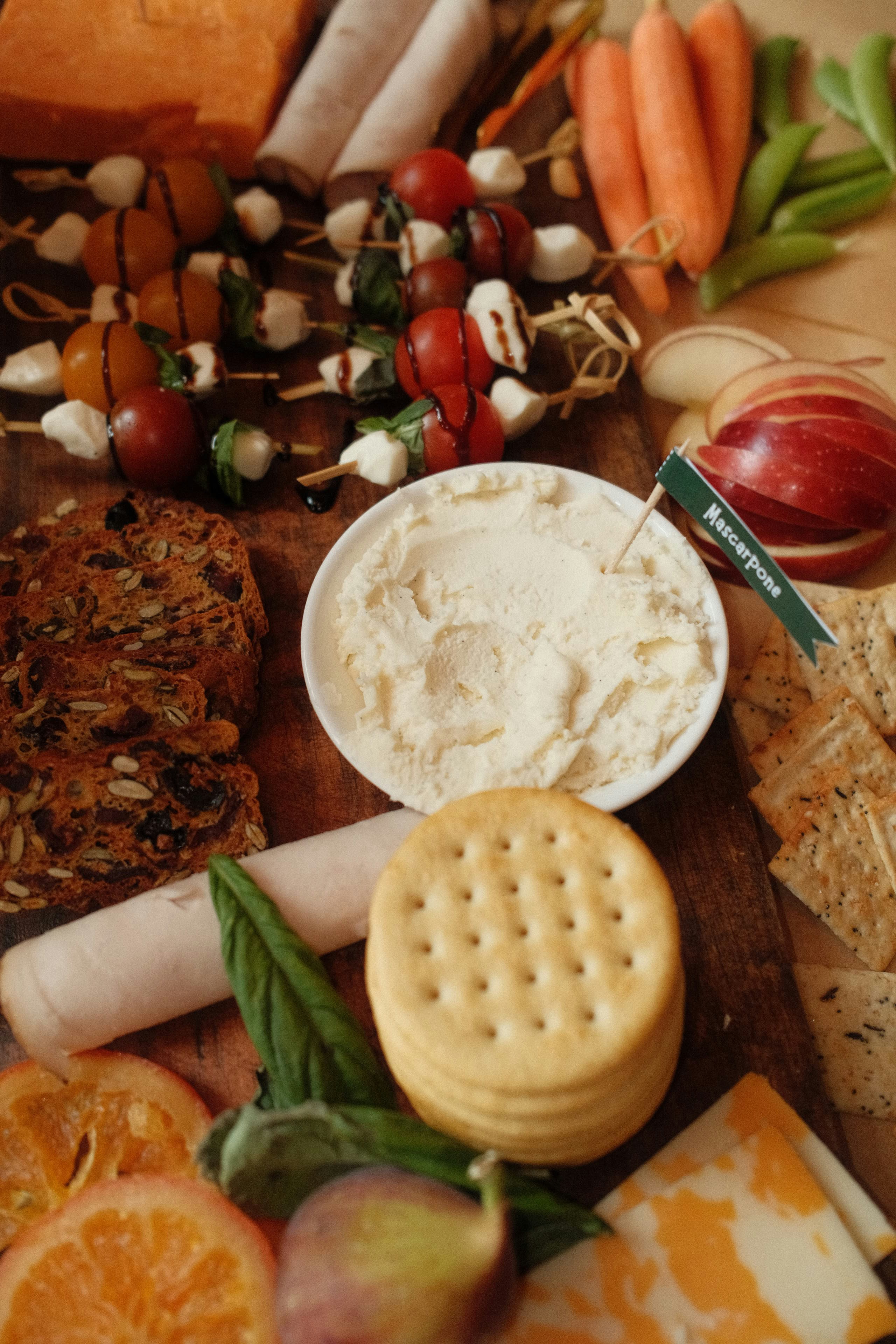 A charcuterie board with mascarpone, crackers, caprese skewers, fruit, and vegetables