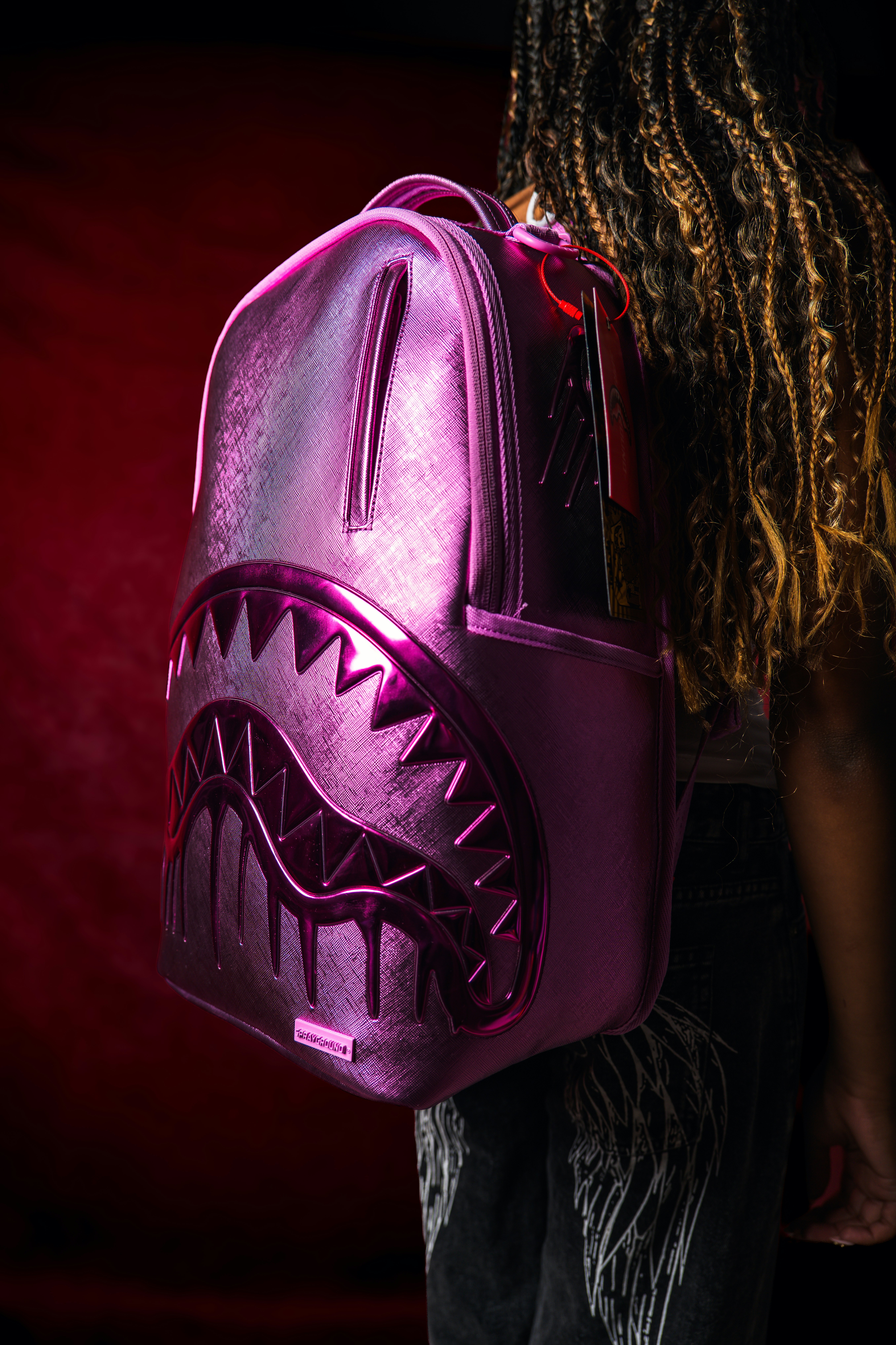 A person with long braided hair wearing a metallic pink shark backpack