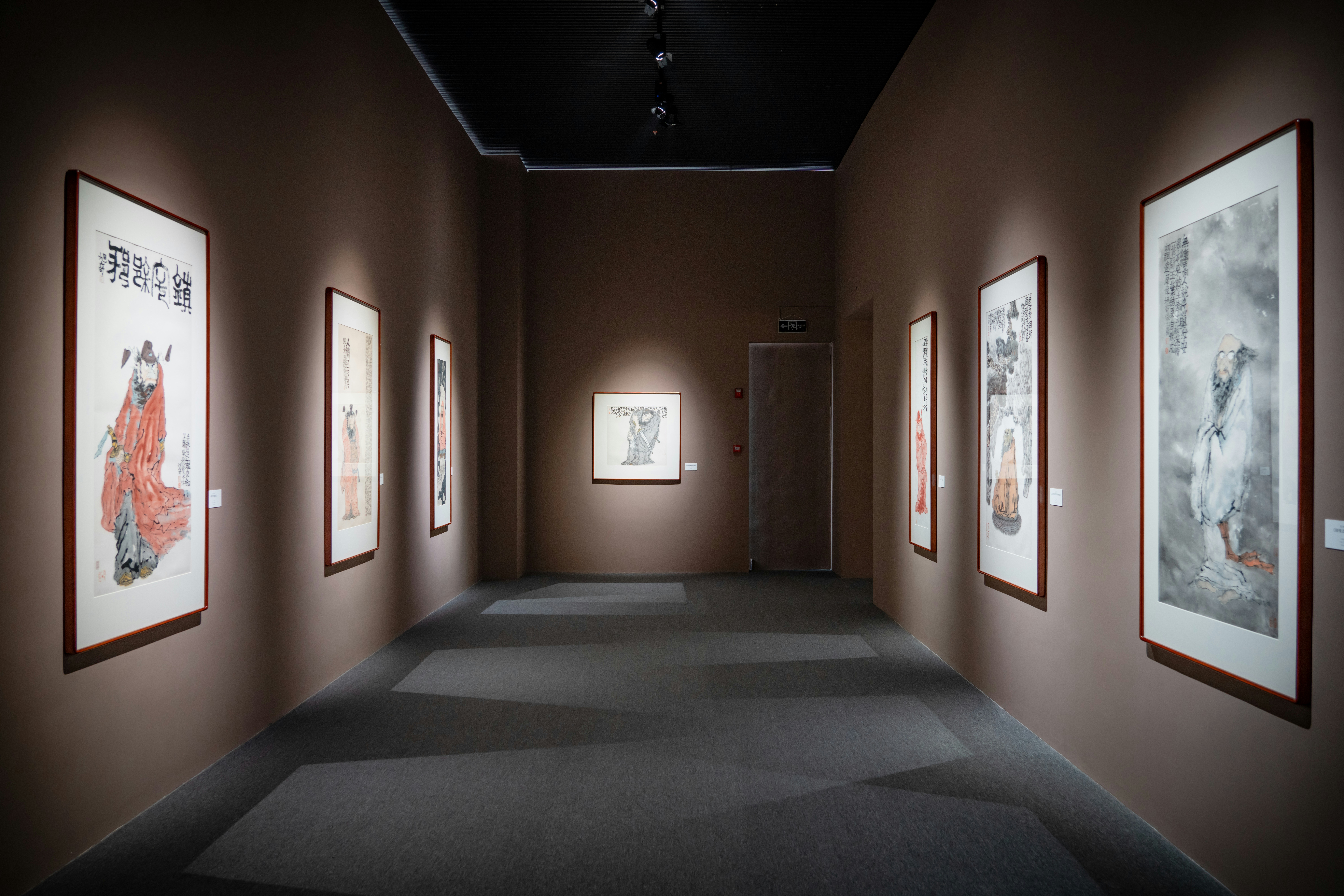 Framed traditional ink paintings hanging on the brown walls of a quiet art gallery