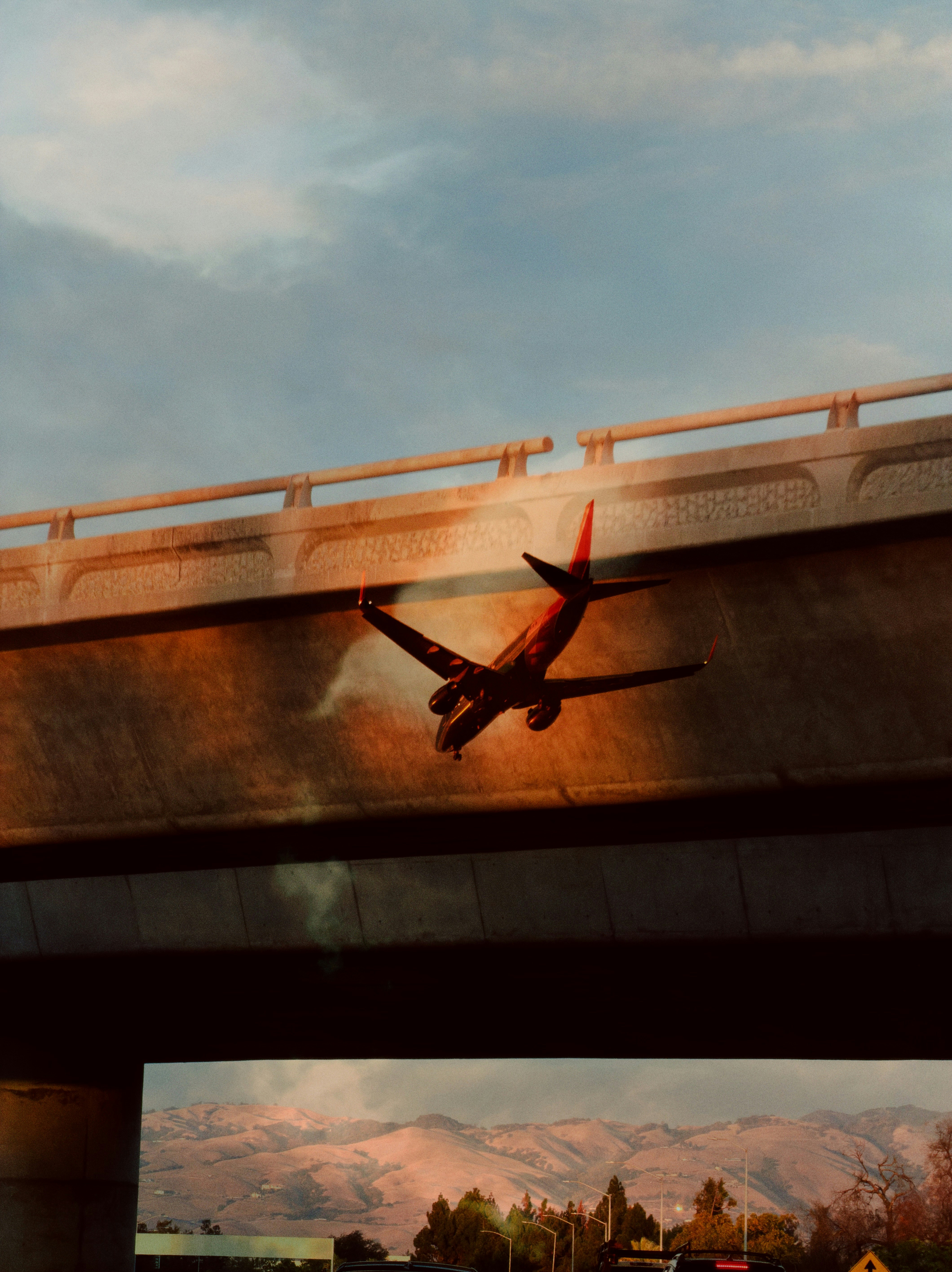 A passenger airplane flying low beneath a concrete highway overpass at golden hour