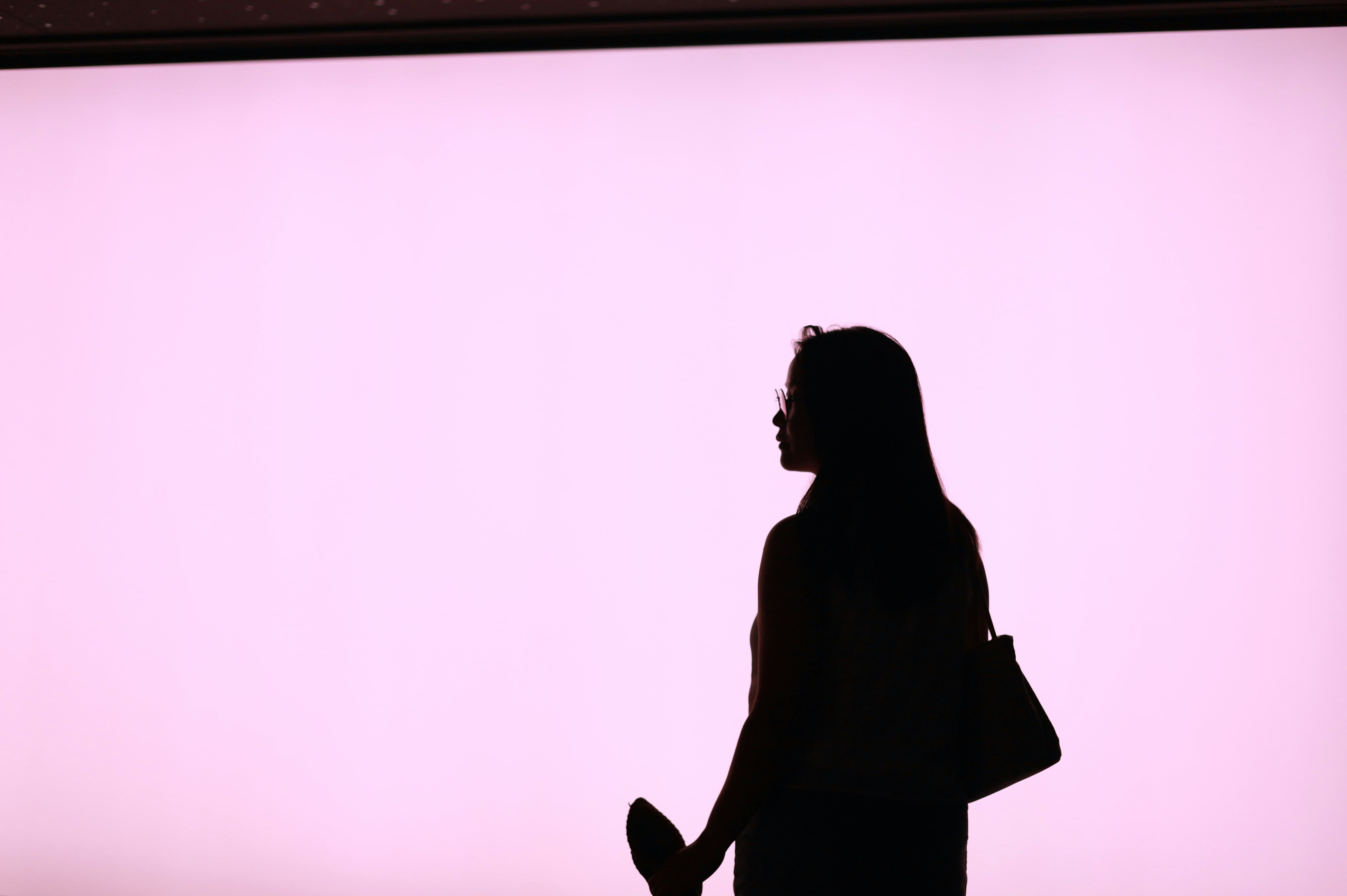 A woman in silhouette against a bright pink background, carrying a shoulder bag