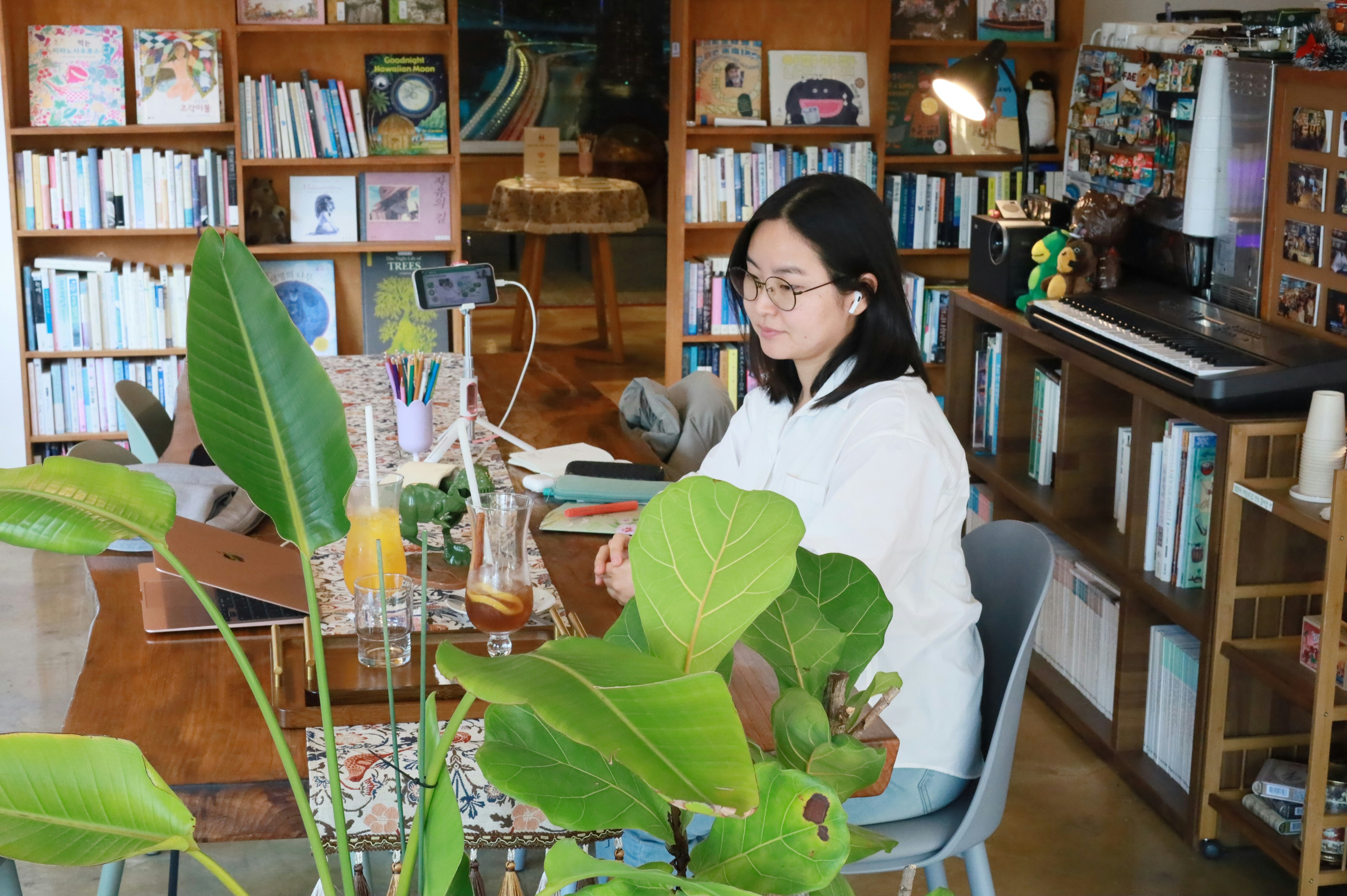 Woman working at a wooden table among plants and books