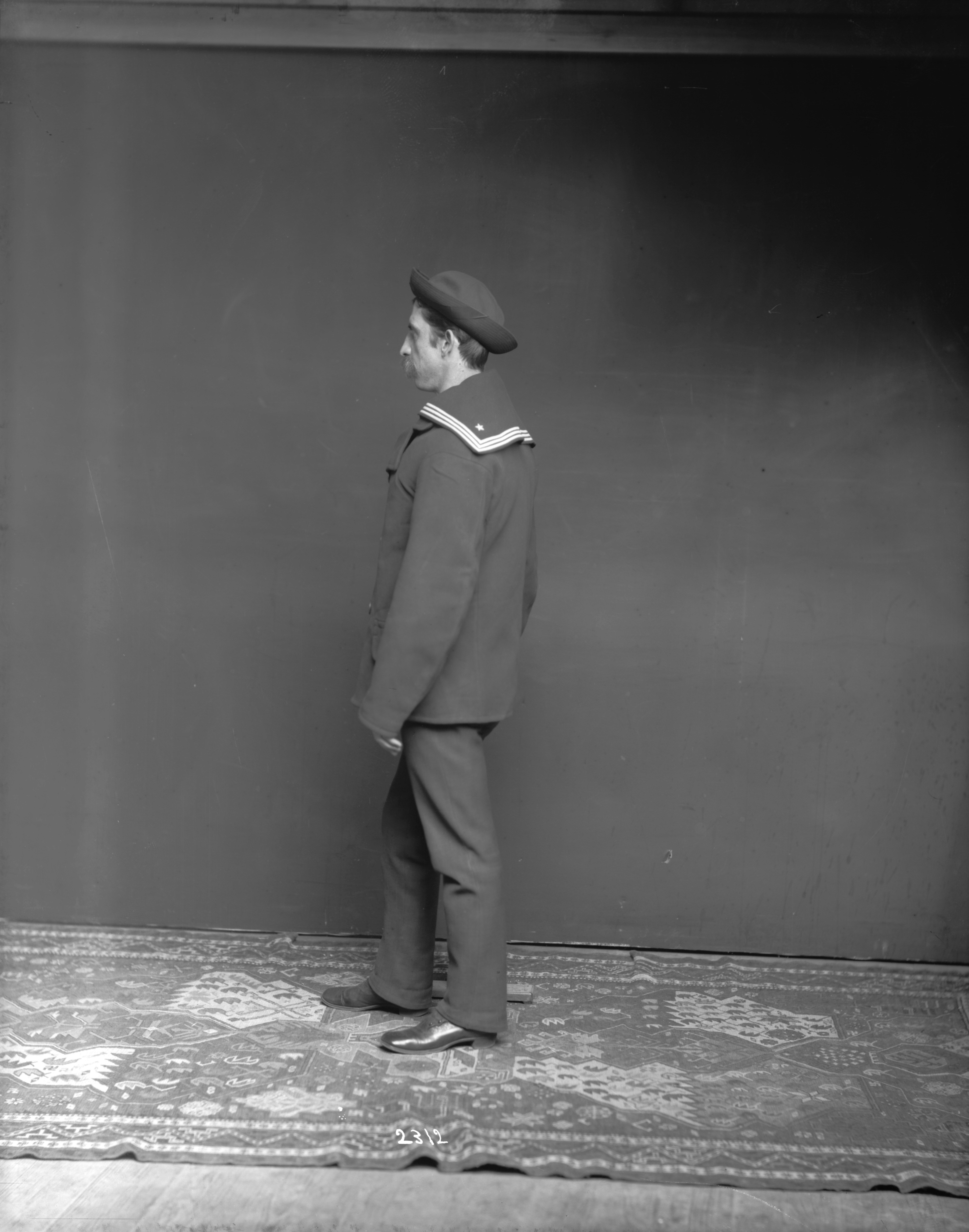 A man in a navy uniform and cap on a patterned rug