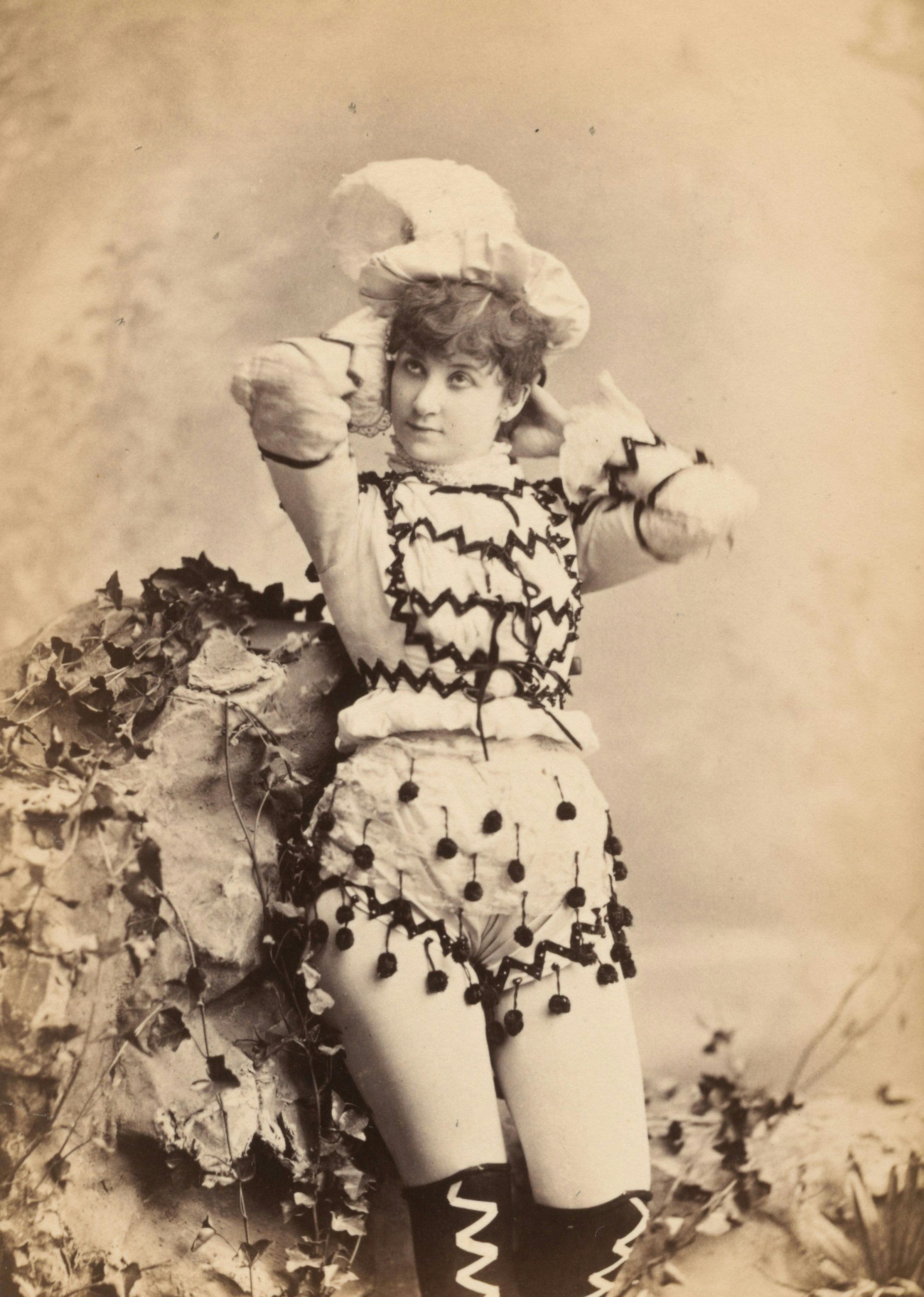 A woman in a vintage costume with pom-poms leaning against a rock