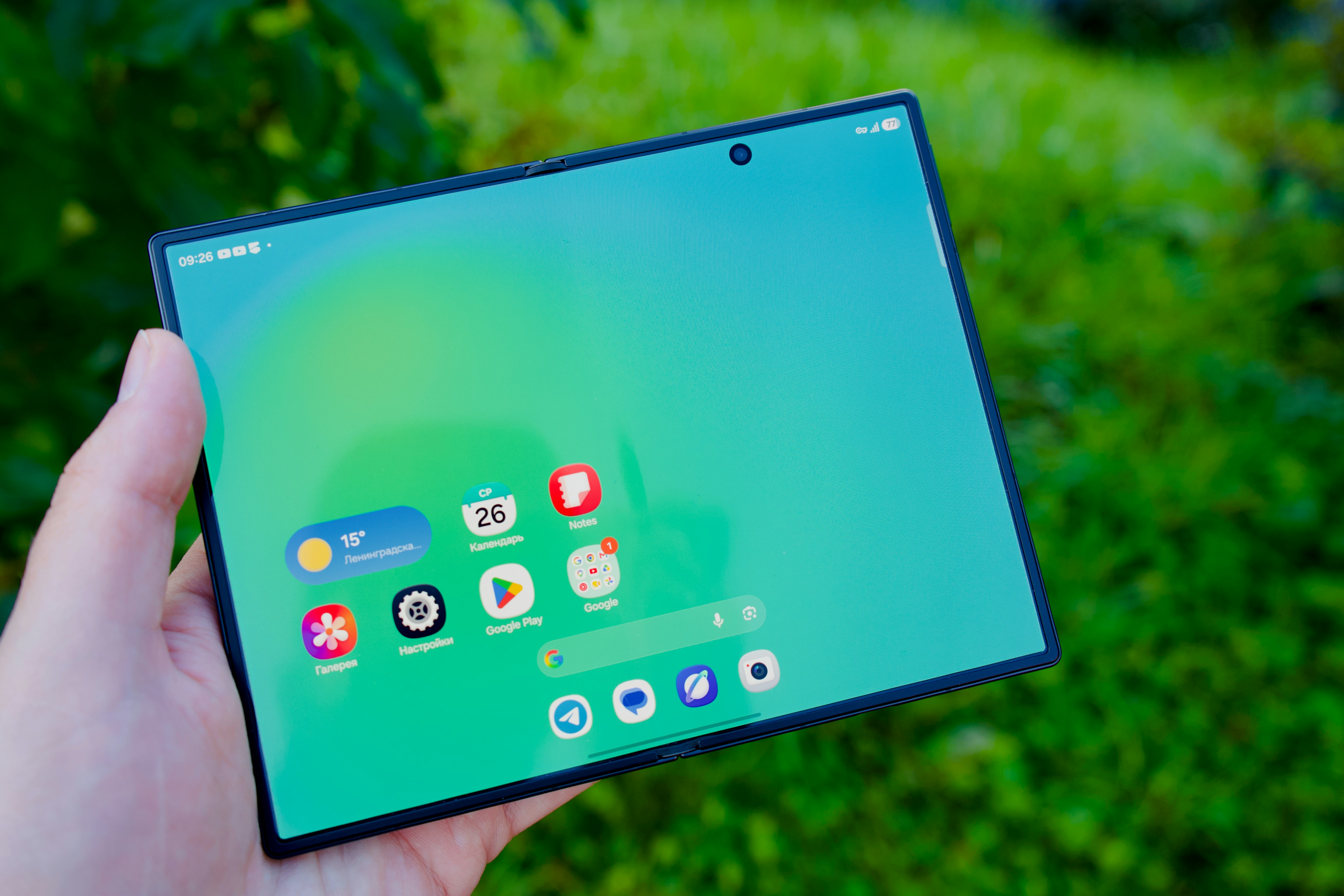 A hand holding a foldable smartphone with a green screen and app icons
