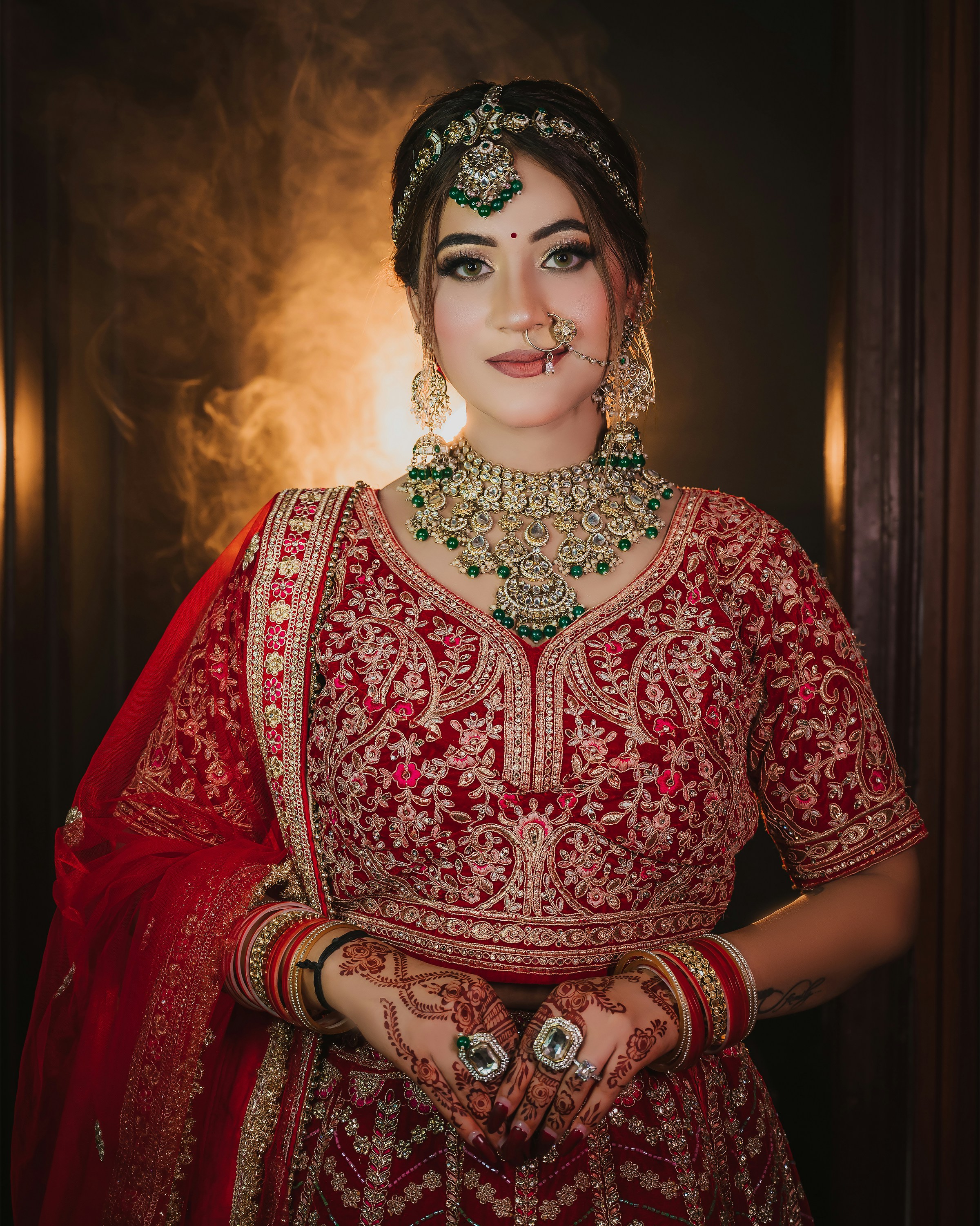 A woman in a red embroidered lehenga with gold jewelry and henna patterns