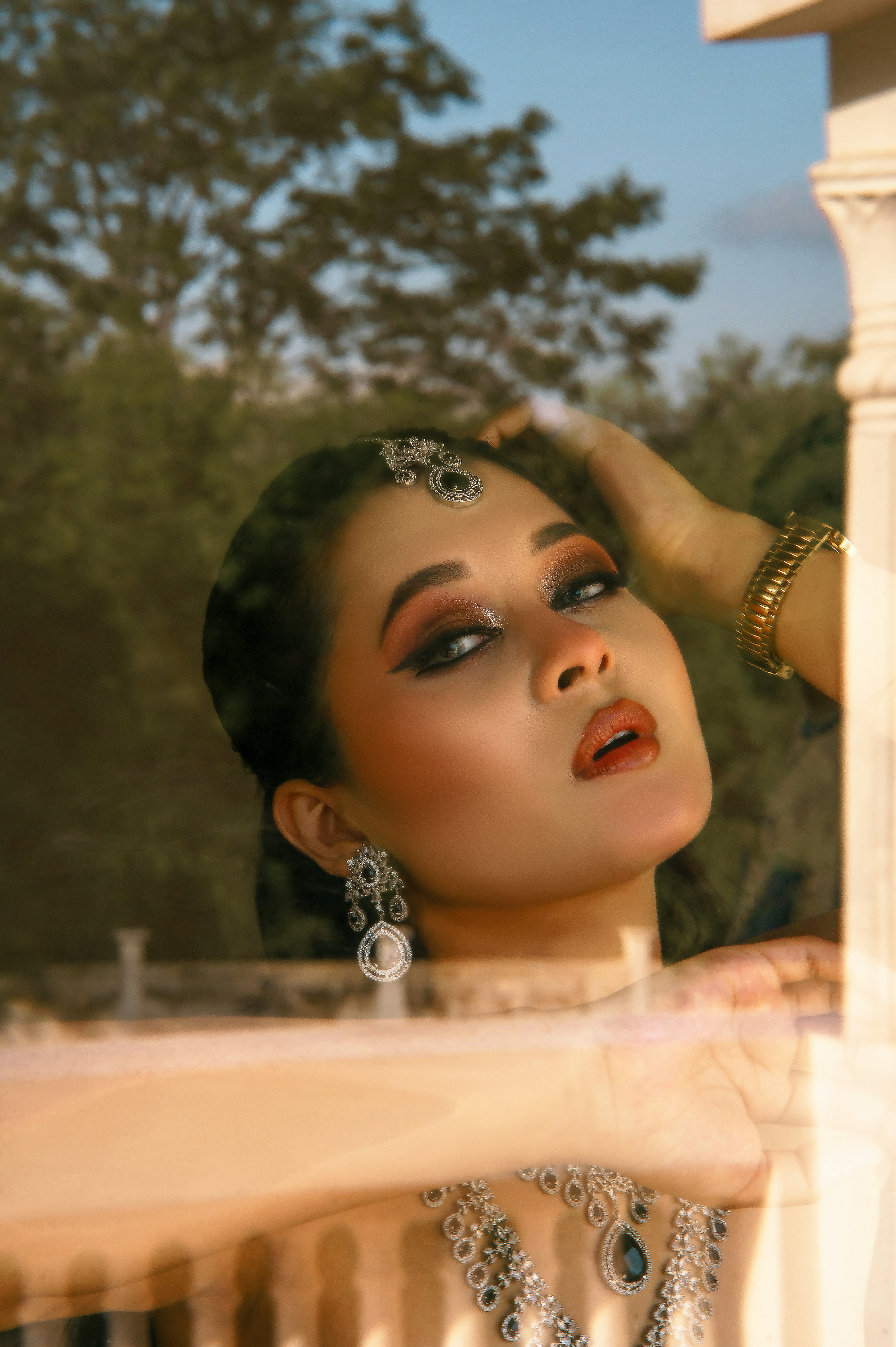 A woman wearing ornate silver jewelry and makeup behind a glass window