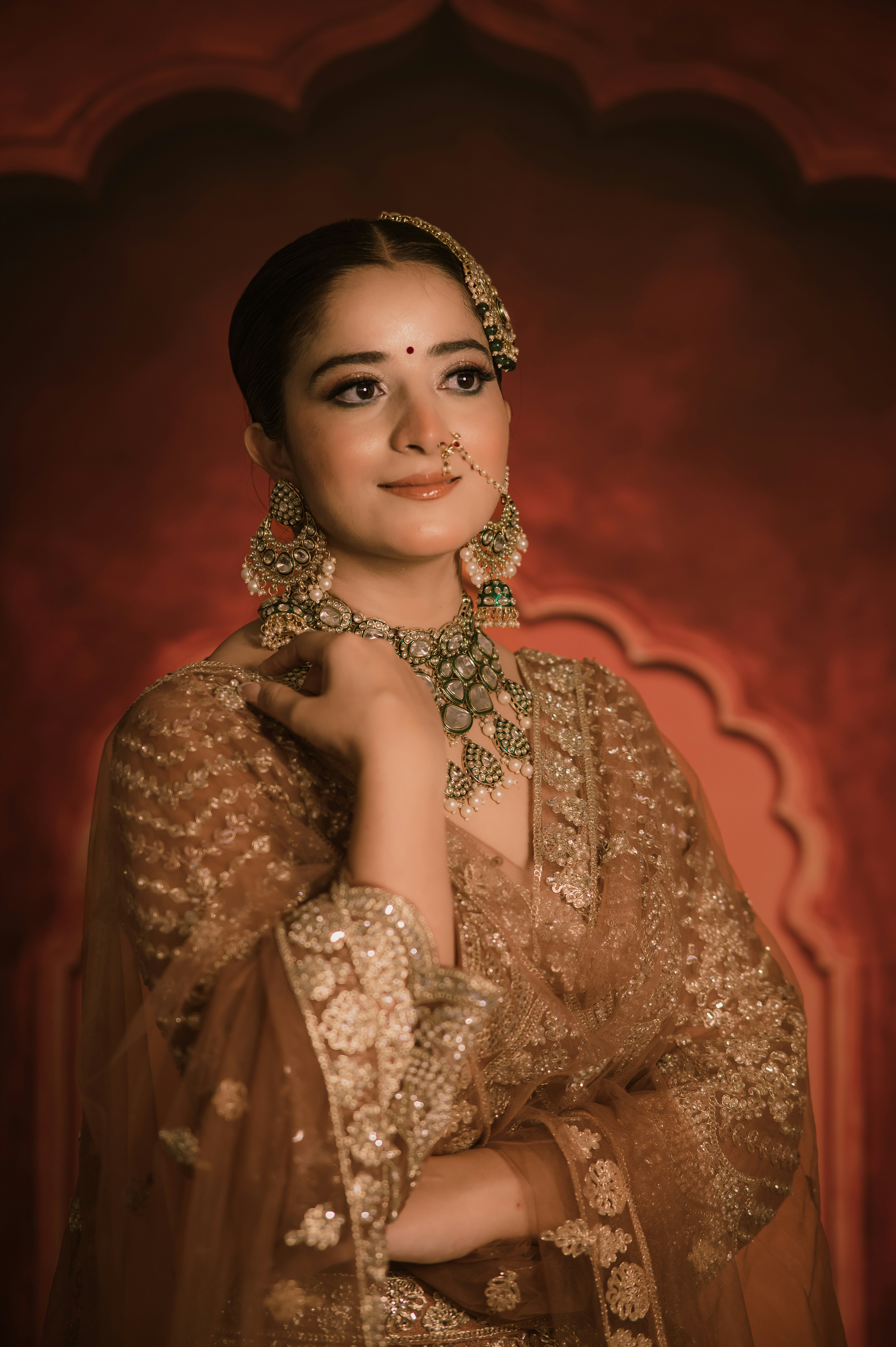 A woman wearing a gold embroidered lehenga and traditional jewelry against a red background