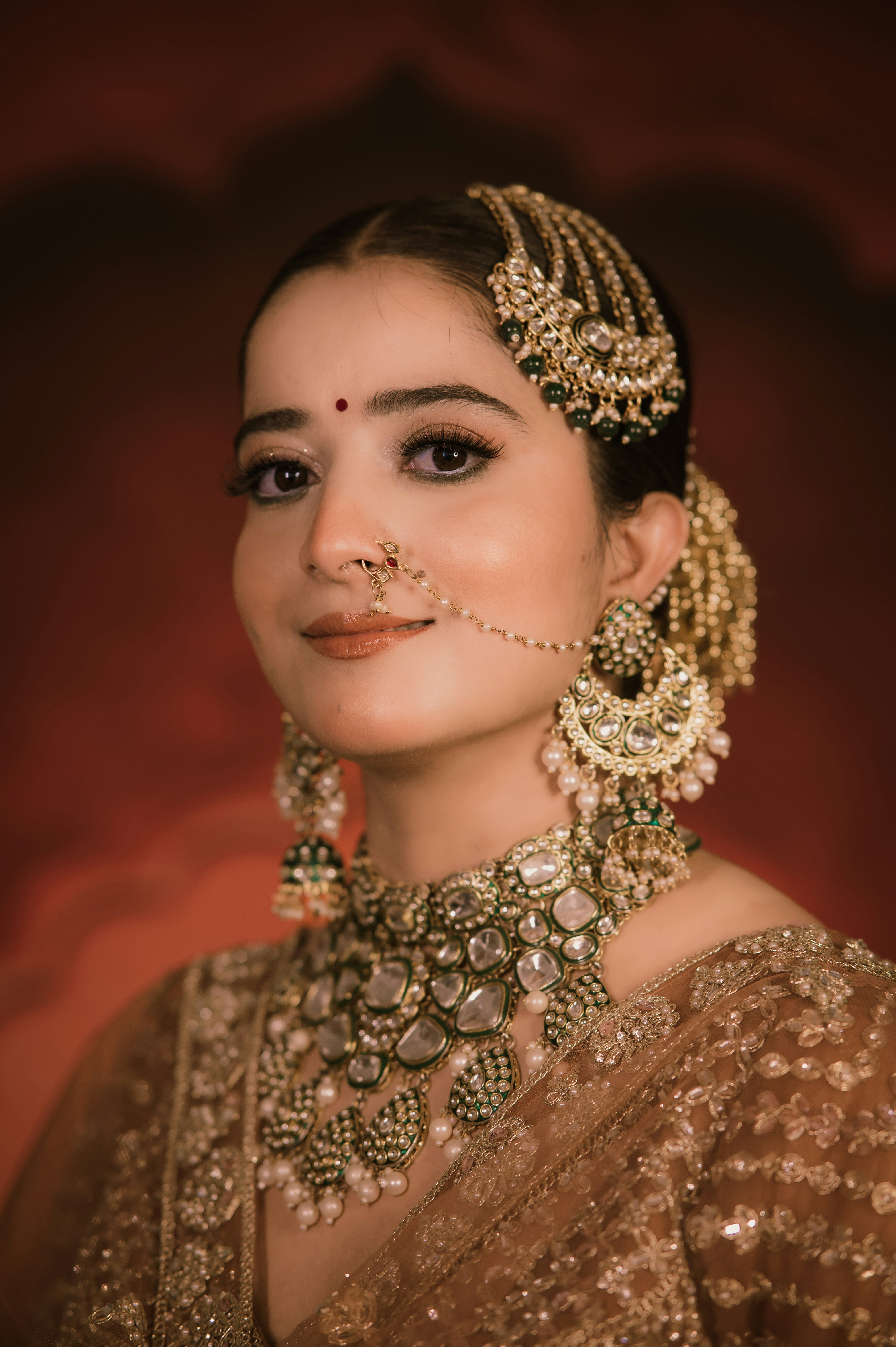 A woman wearing ornate gold jewelry and a nose ring against a red background