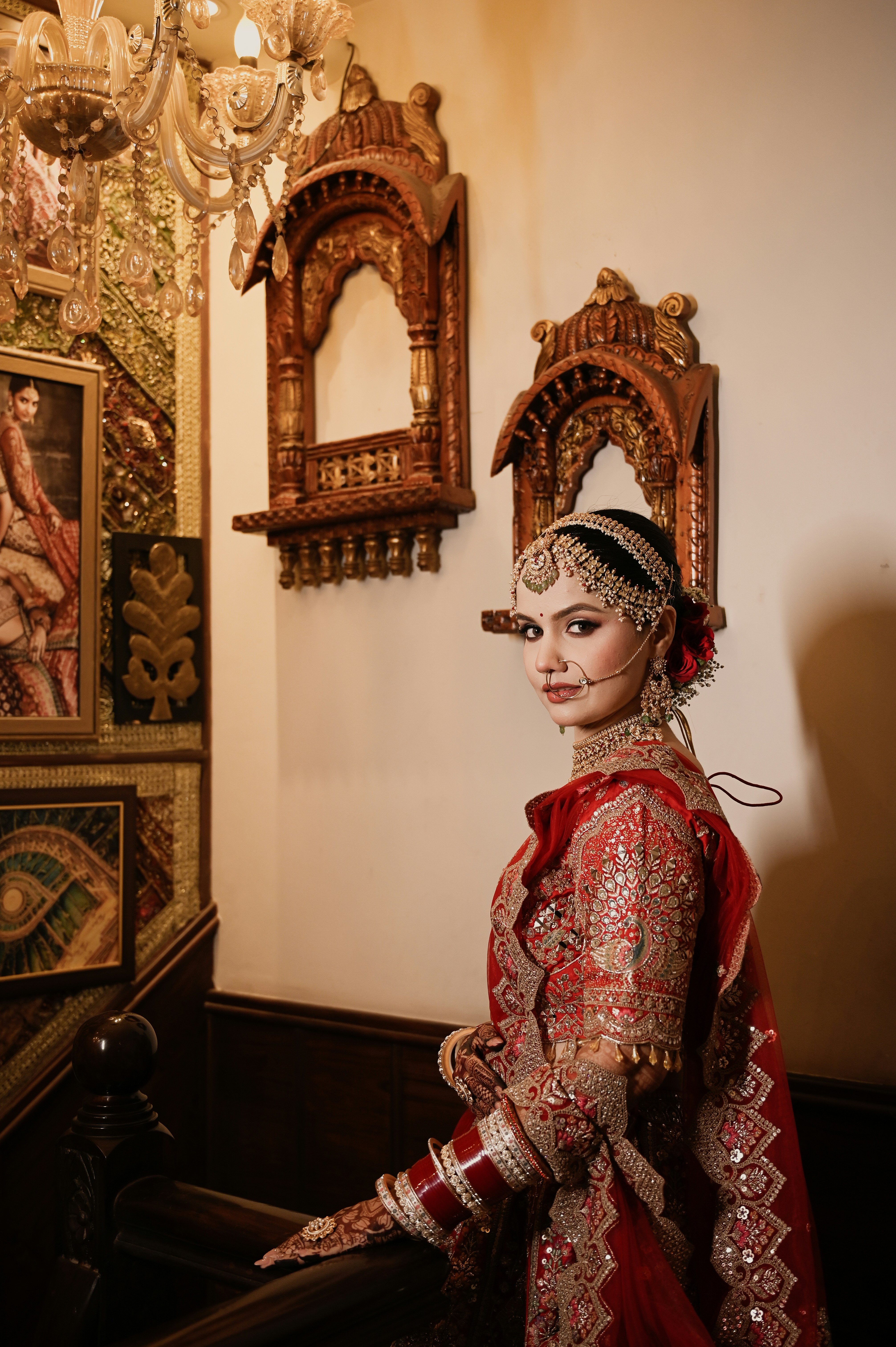 A woman in a red embroidered bridal lehenga and traditional jewelry in a room