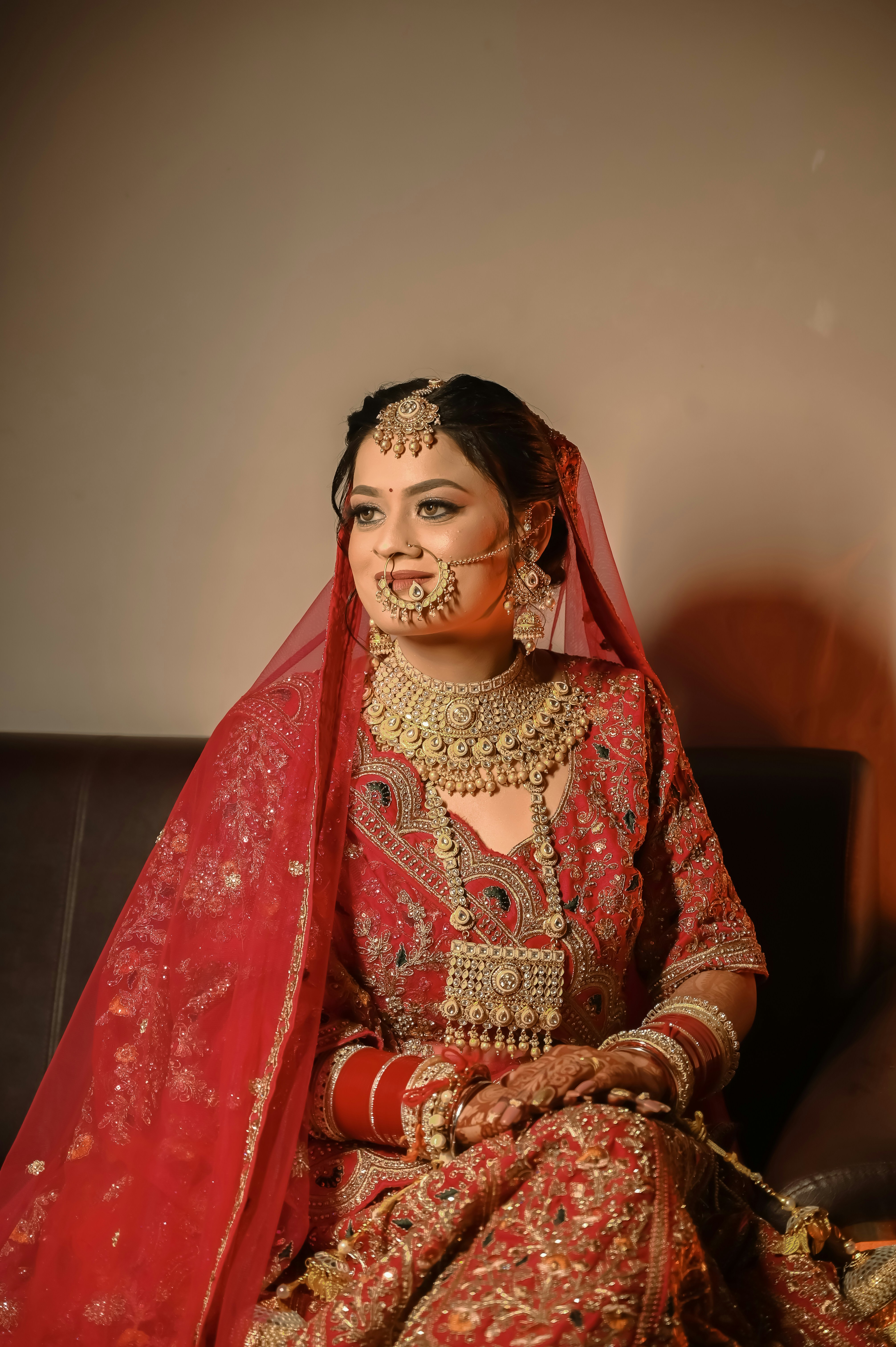 A woman in a red embroidered bridal lehenga with heavy gold jewelry and a veil