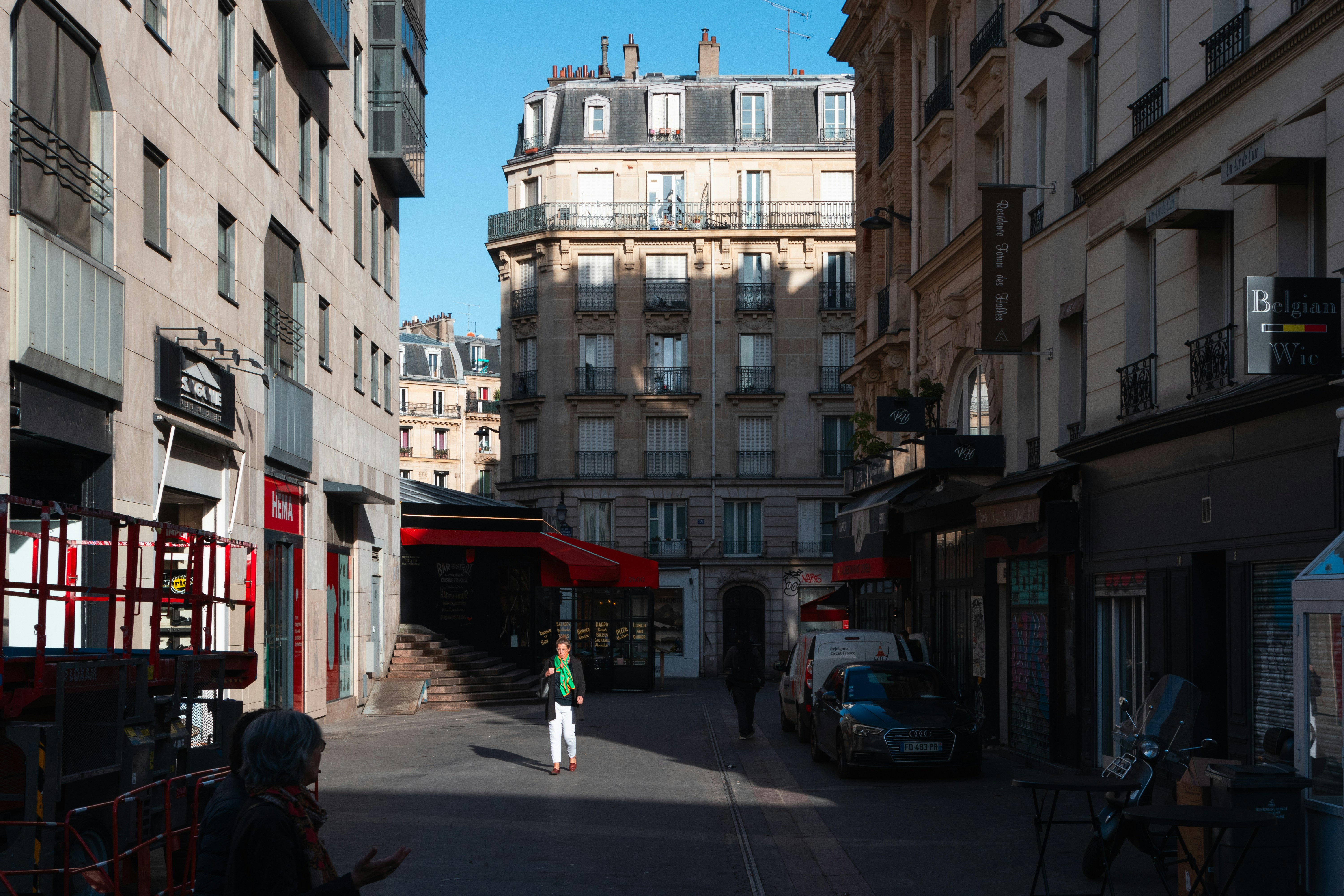 A person walking down a narrow street in Paris lined with shops and apartments