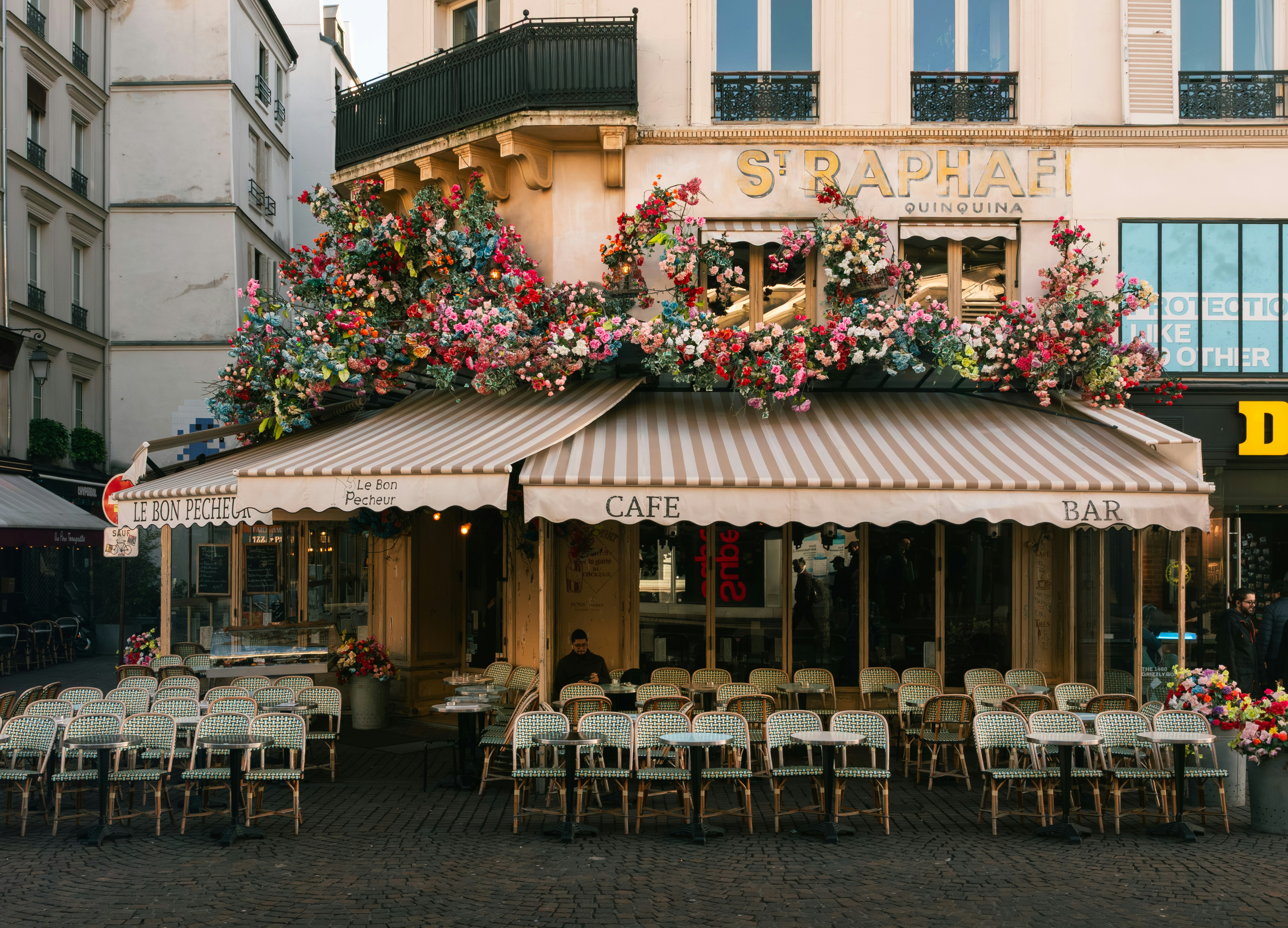 A cafe with a striped awning and floral decorations on a street in Paris