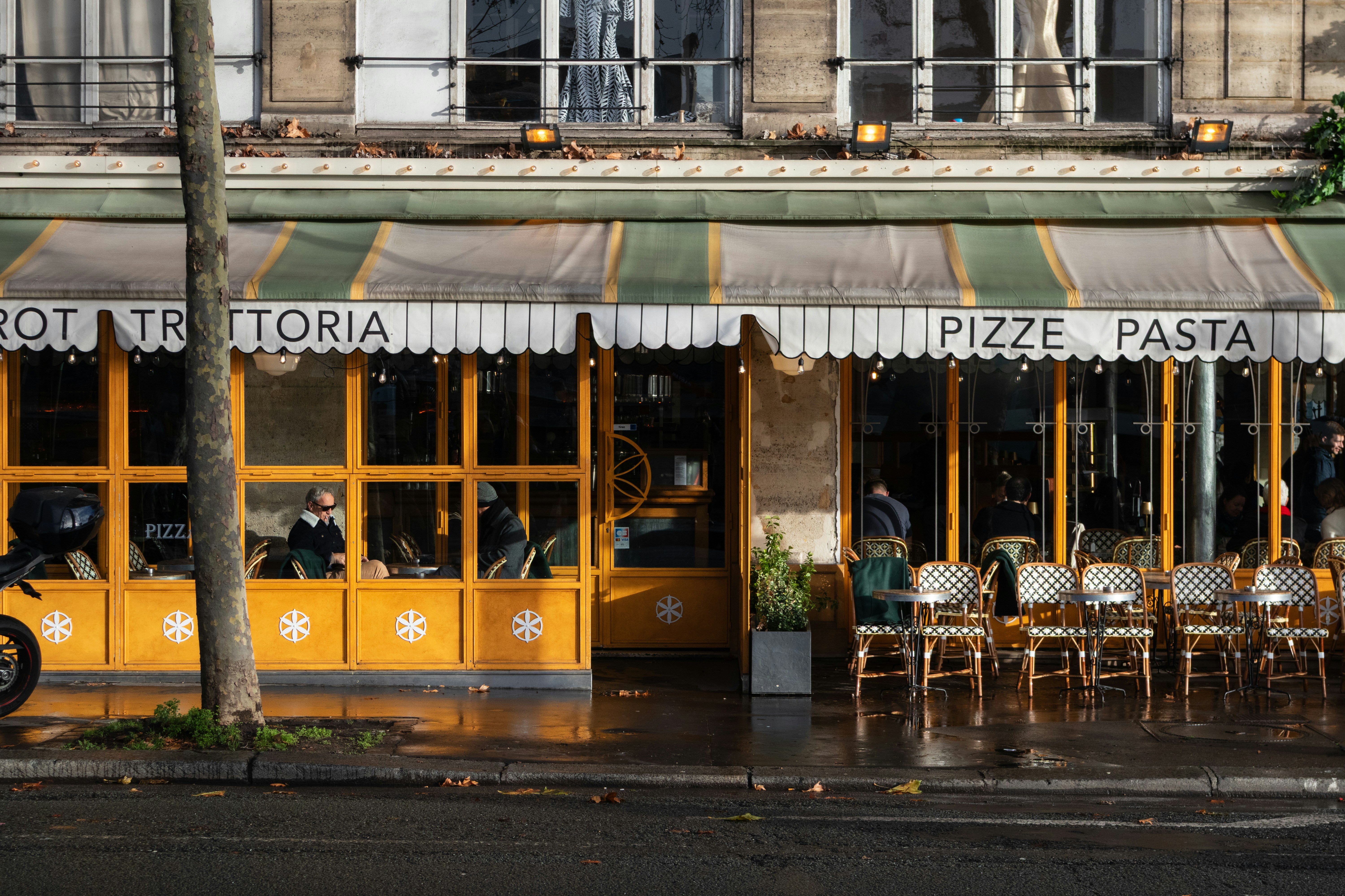 A yellow storefront with outdoor seating and a striped awning in Paris