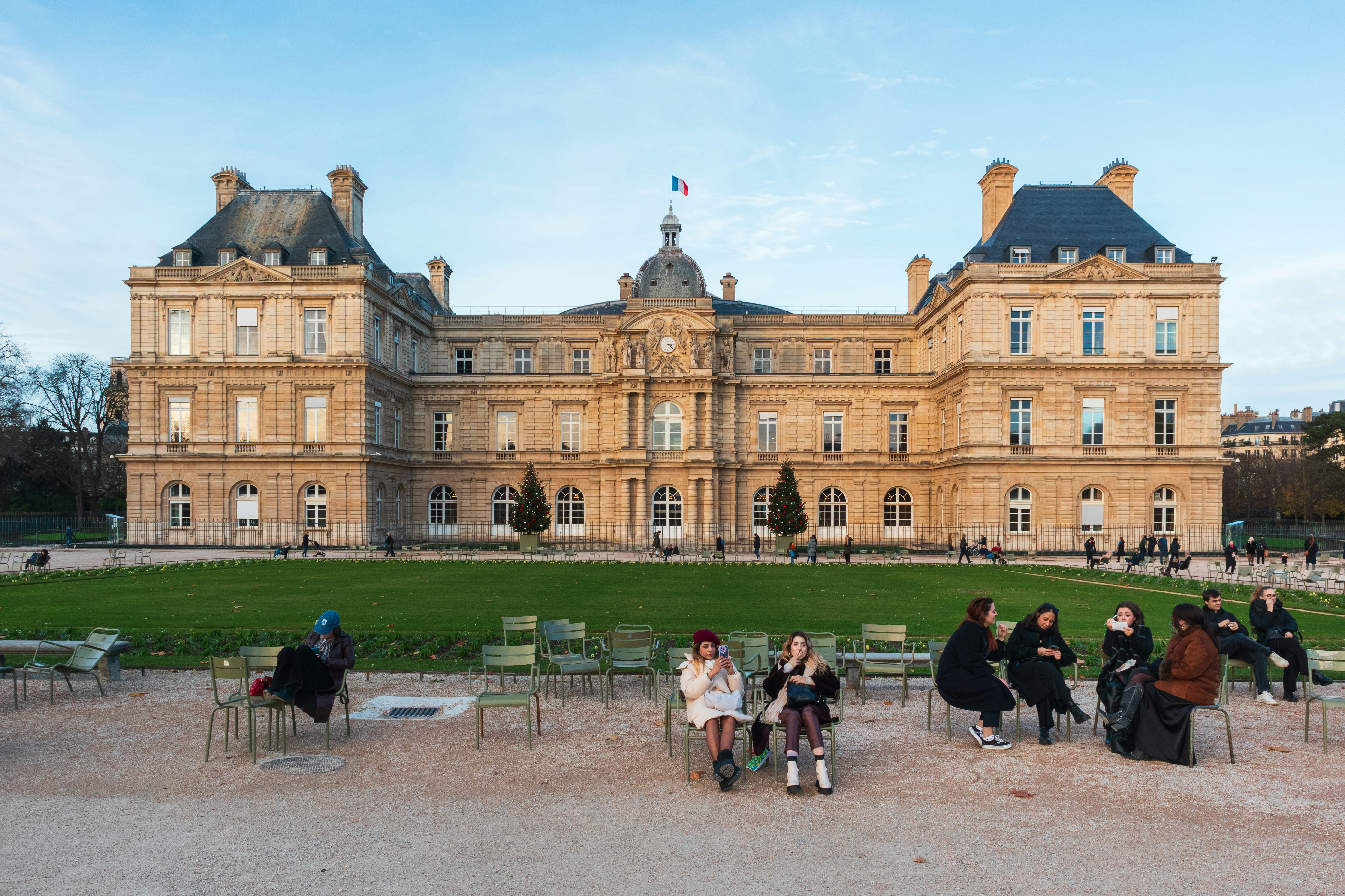 People sitting on green metal chairs in front of the Luxembourg Palace in Paris