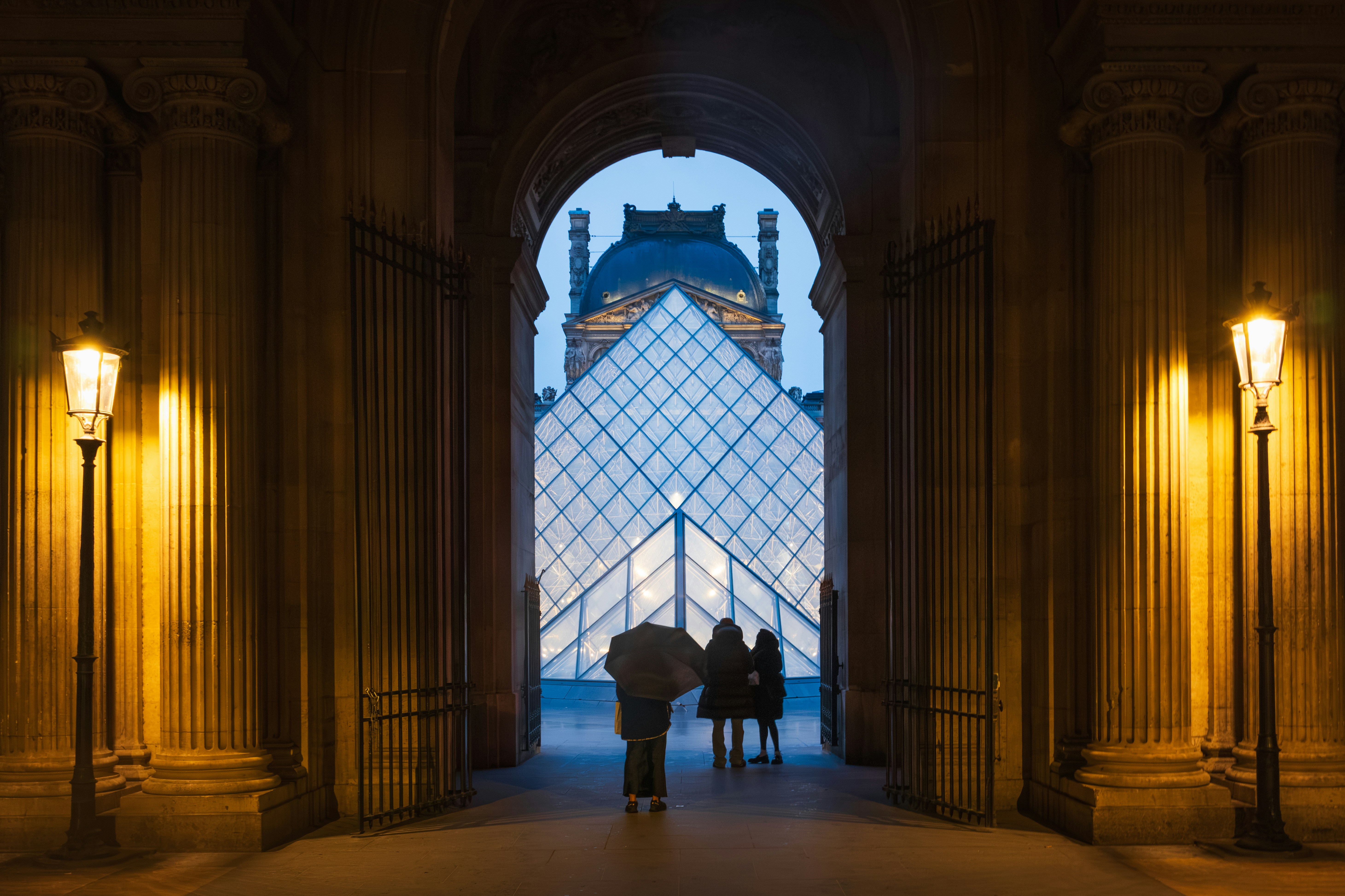 People with an umbrella looking at the Louvre Pyramid in Paris at night