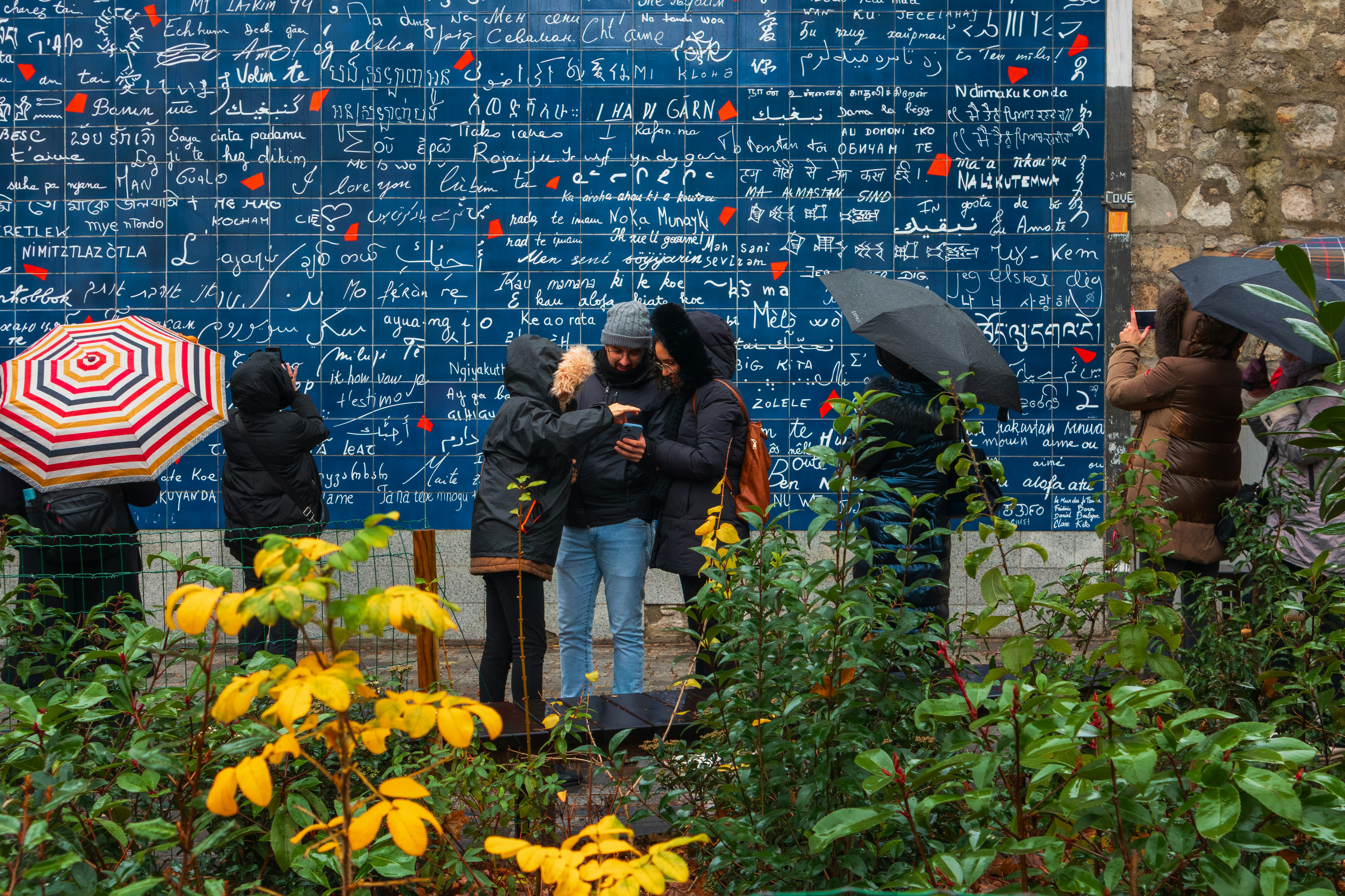 People with umbrellas standing before the I Love You Wall in Paris
