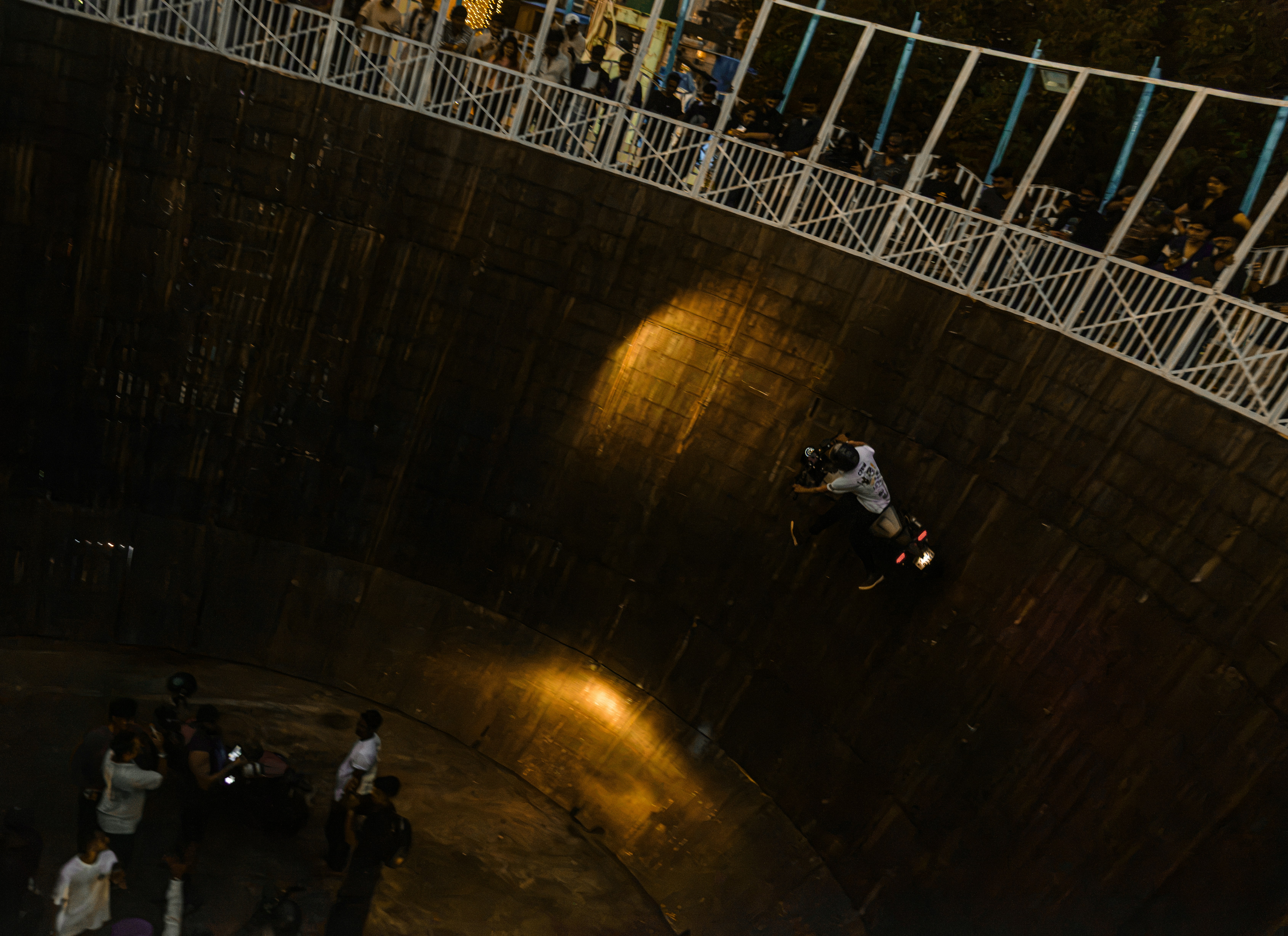 A motorcyclist riding horizontally along the wooden wall of a well of death
