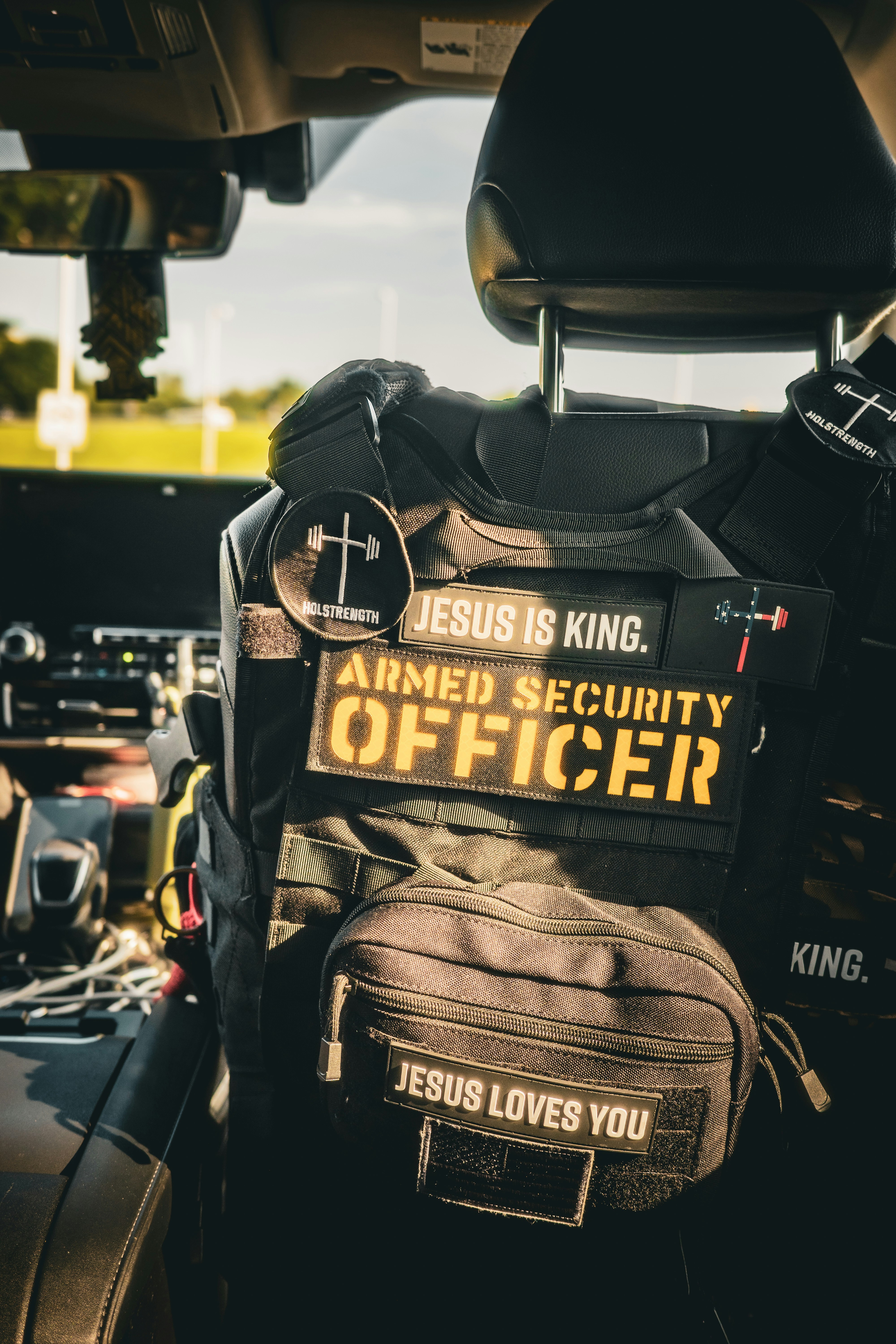 A black tactical vest with patches reading "ARMED SECURITY OFFICER" hanging on a car seat