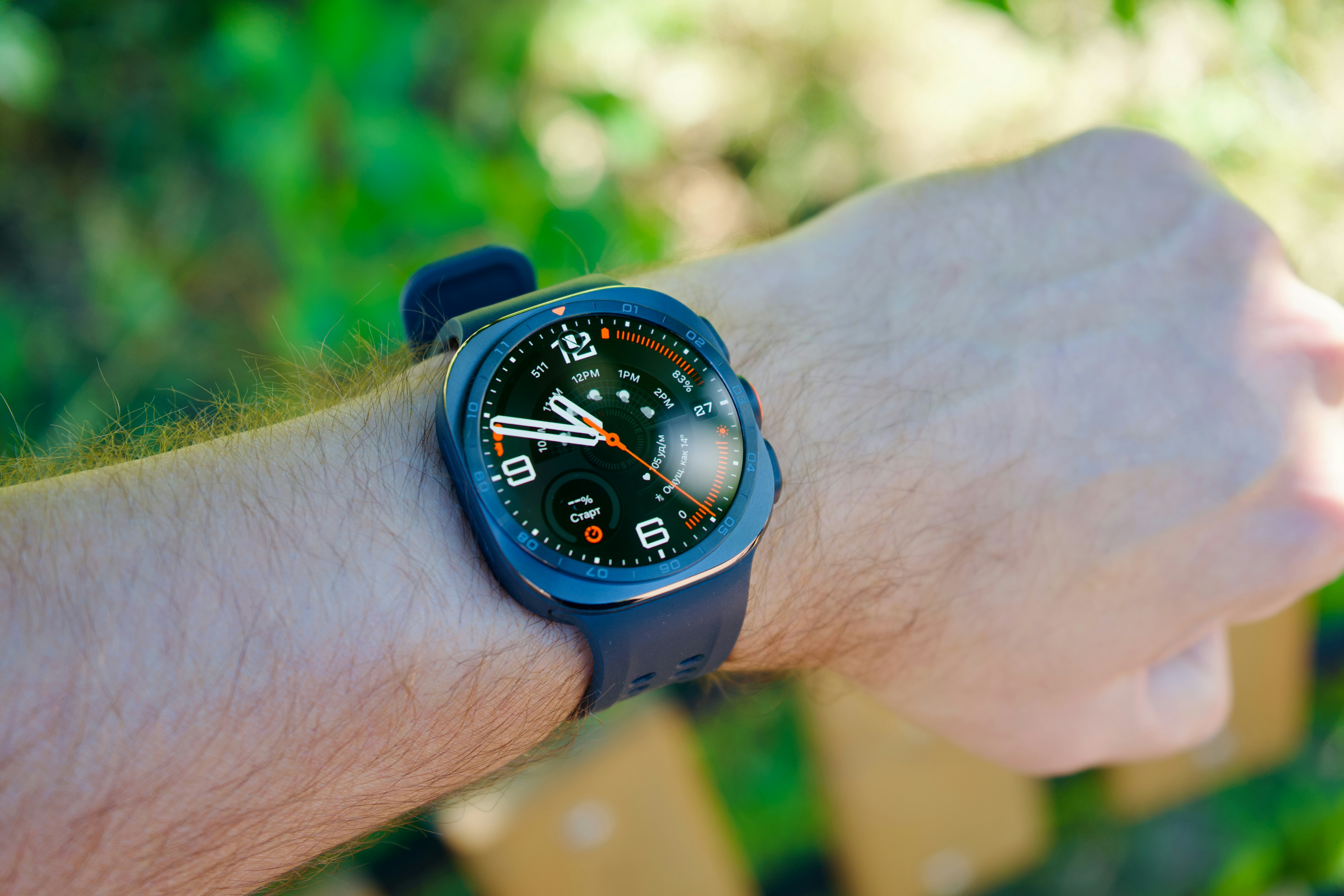 A dark smartwatch with a digital face on a person's wrist outdoors