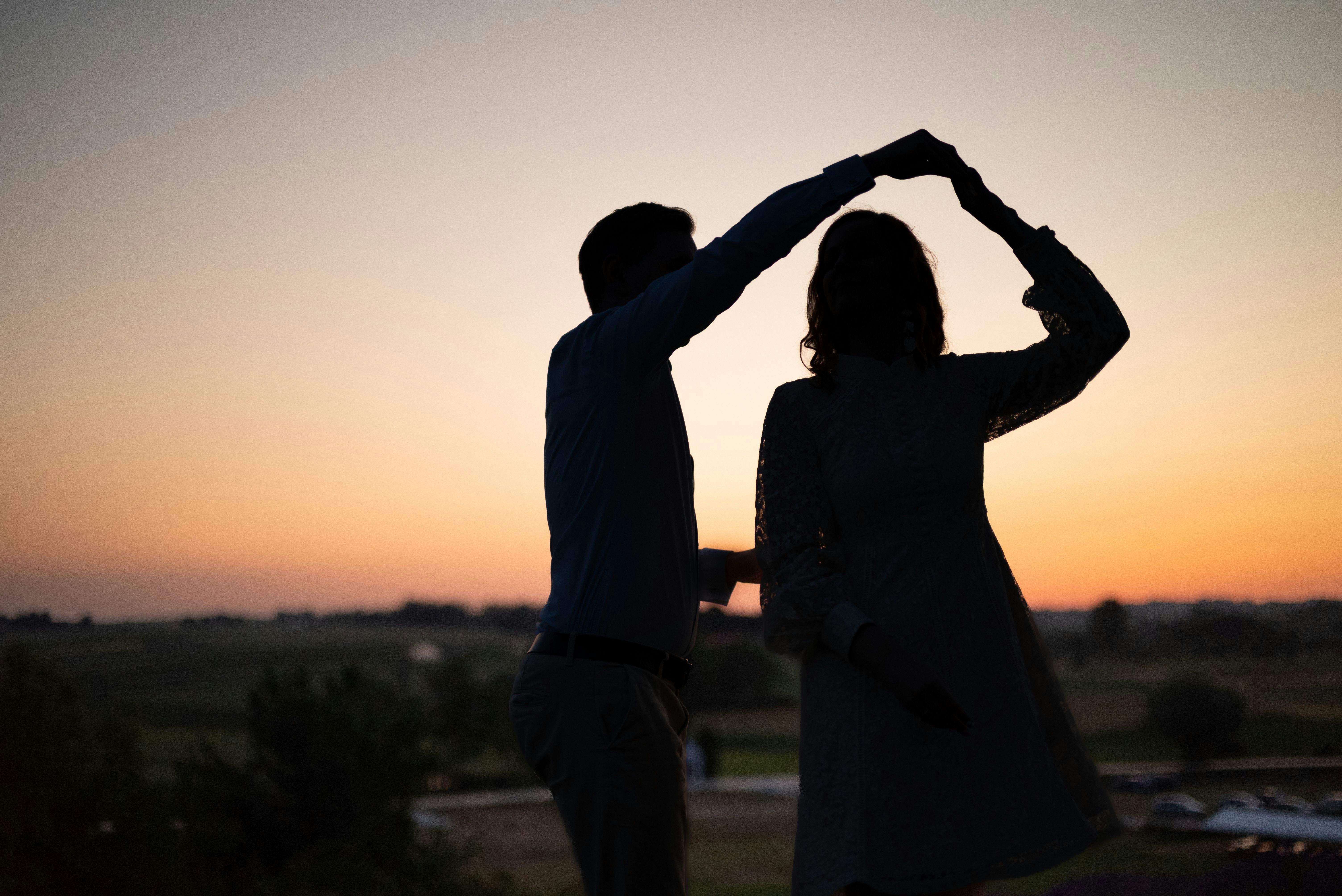 A silhouette of two people dancing against a warm orange sky