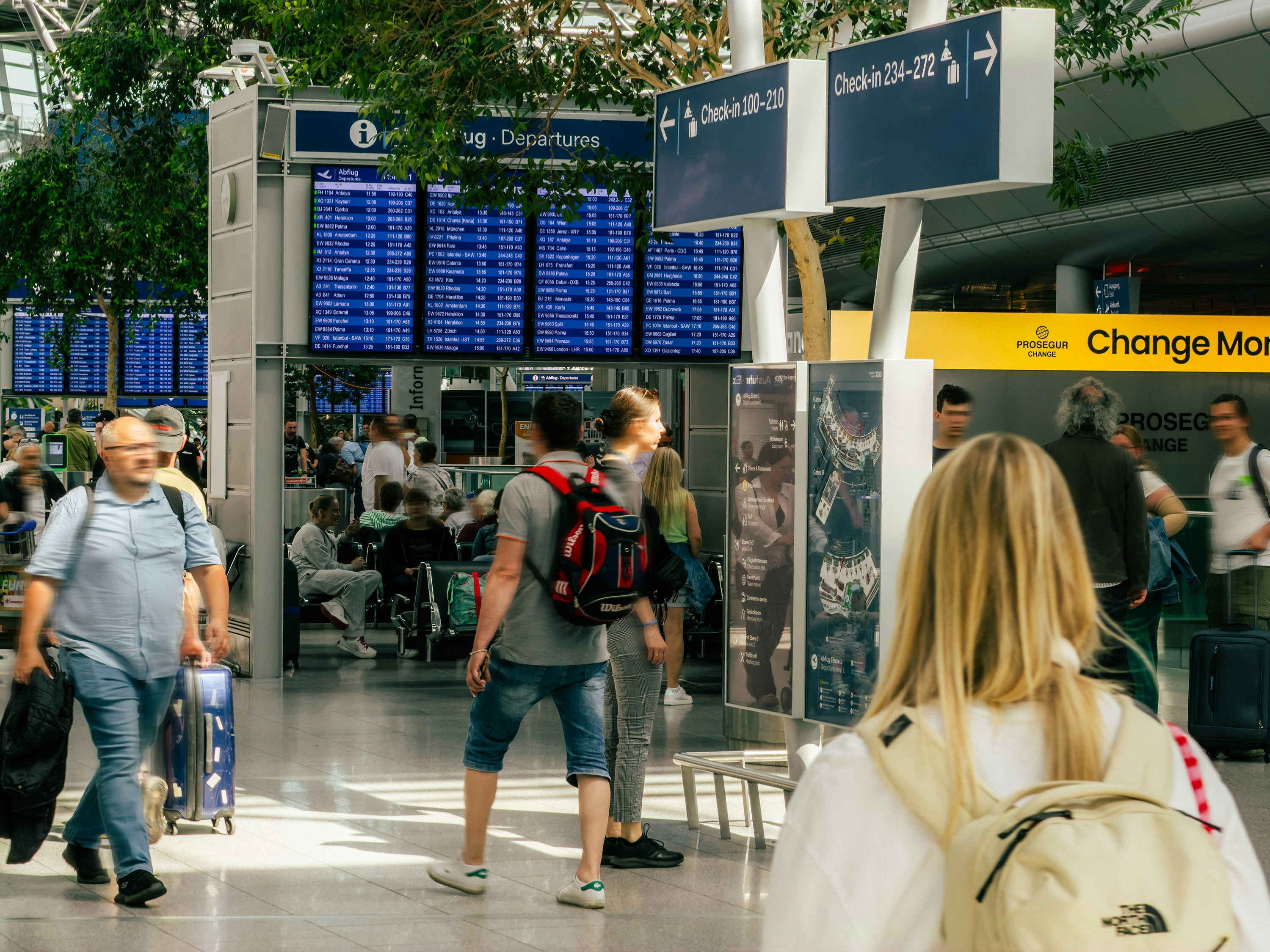 Travellers crossing a departures hall beneath international flight boards