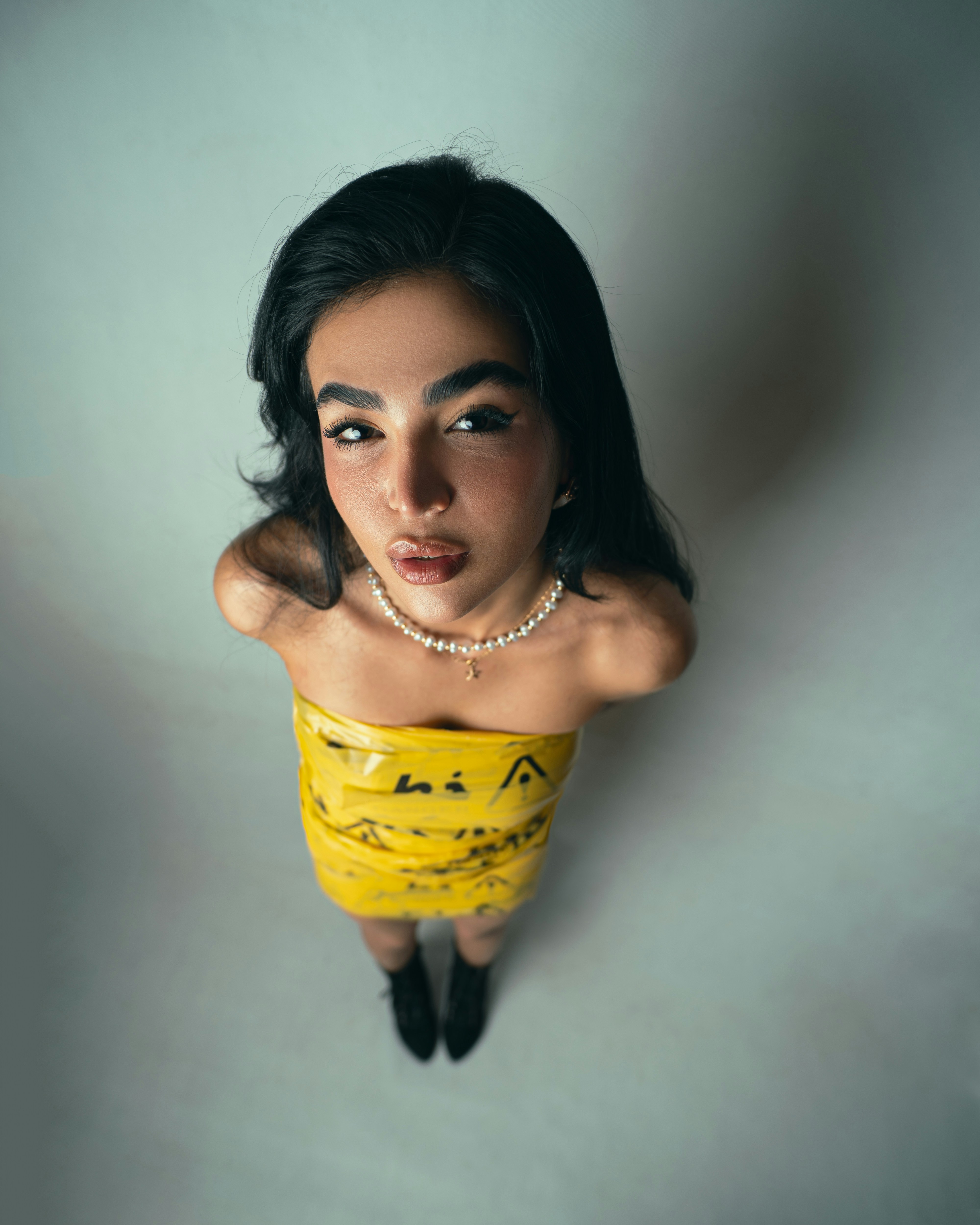 A woman wearing yellow caution tape as a top with a pearl necklace
