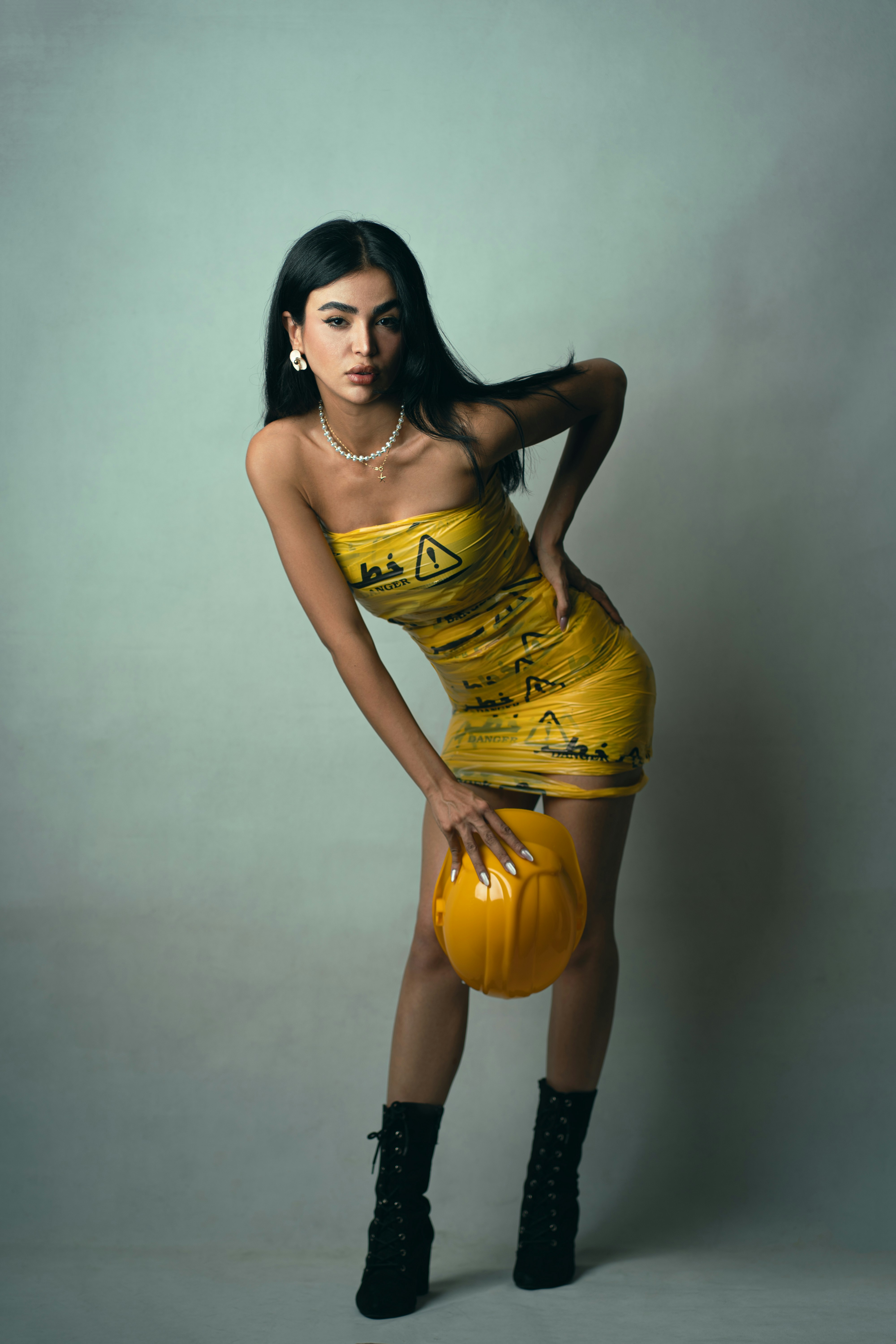 A woman wearing a yellow caution tape dress holding a yellow hard hat
