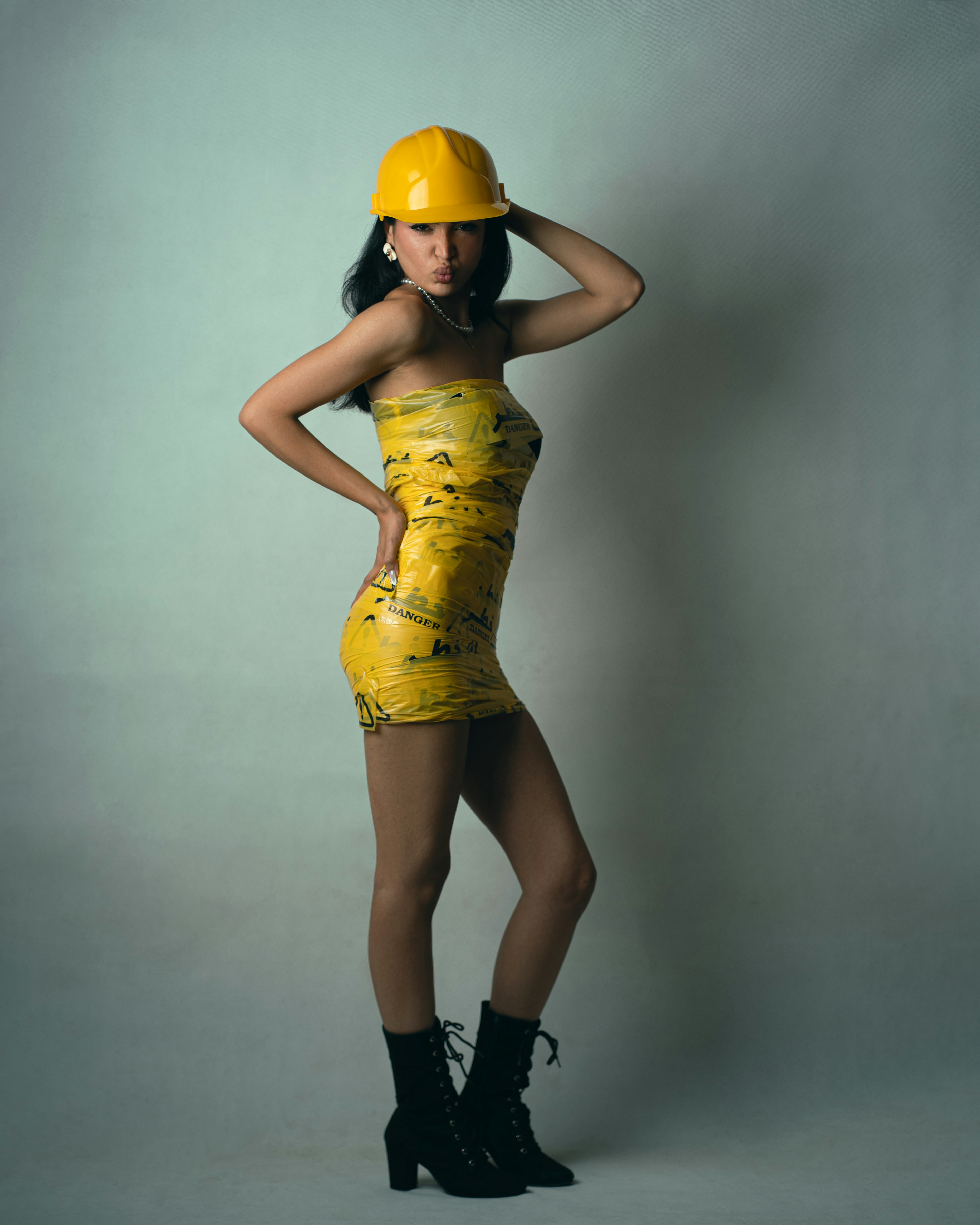 A woman wearing a yellow hard hat and a dress made of caution tape