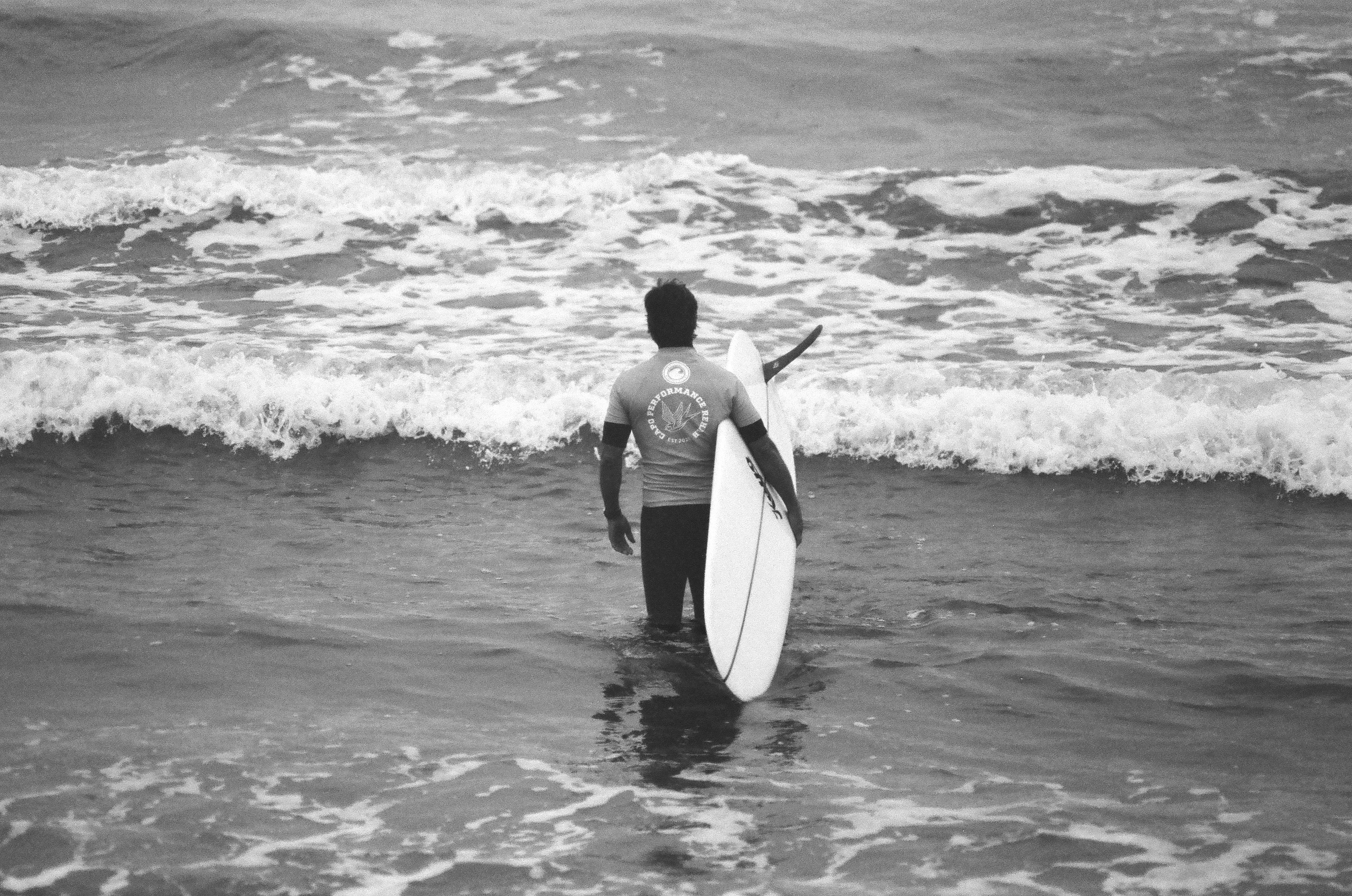 A person in a wetsuit carrying a surfboard into the ocean waves