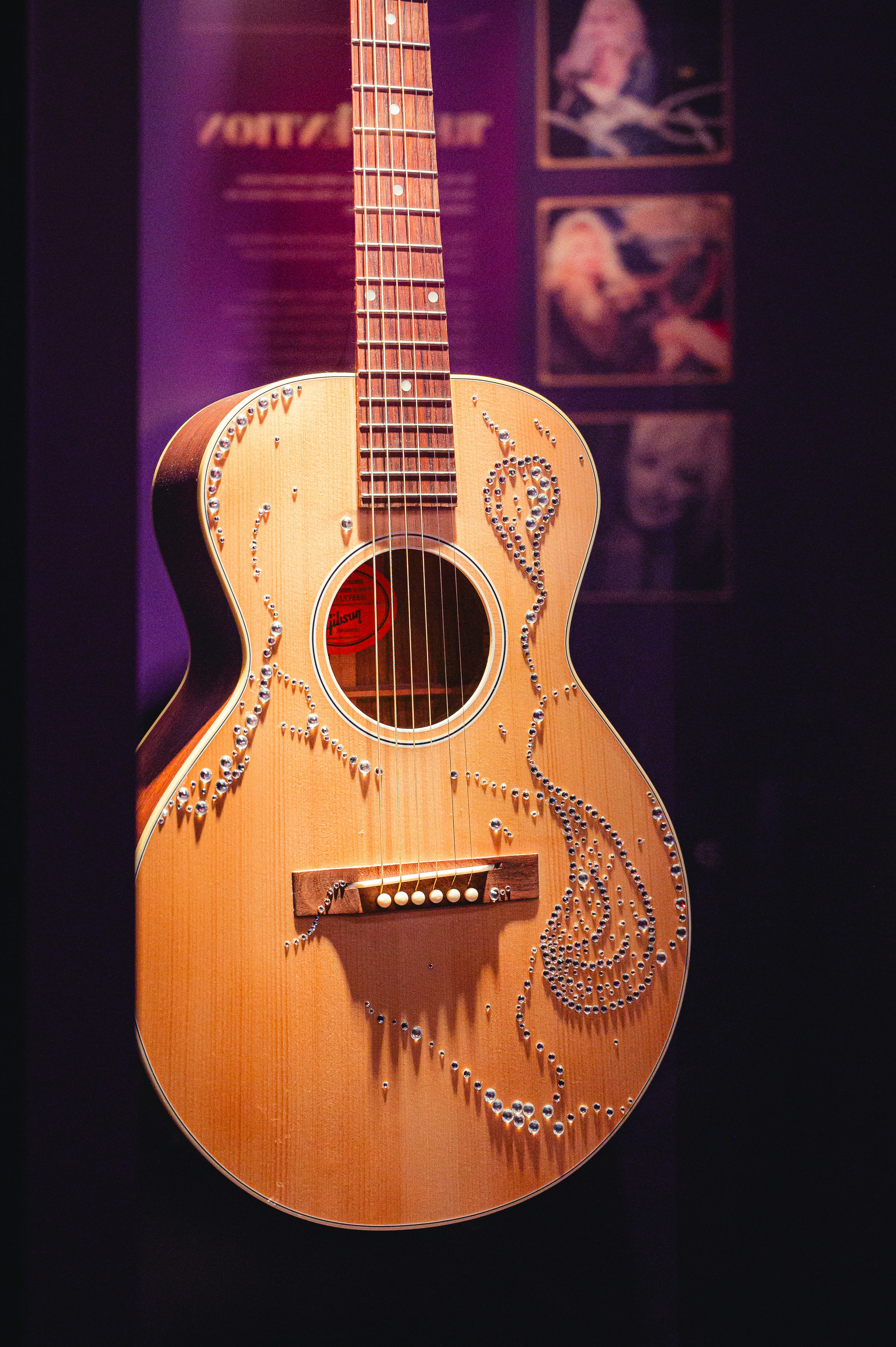 A light wood acoustic guitar decorated with rhinestones in a swirling pattern