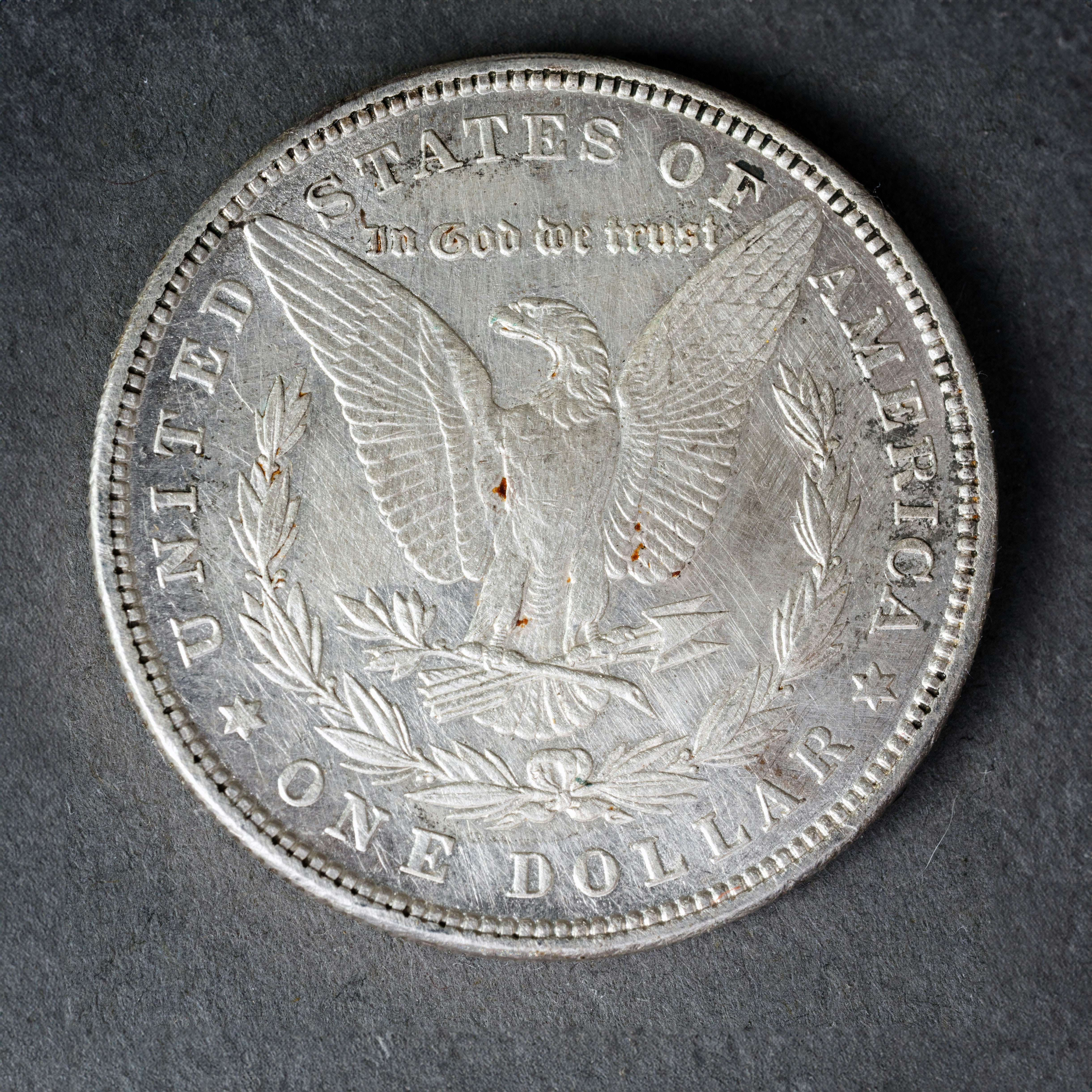 A silver United States one dollar coin with an eagle on a dark surface