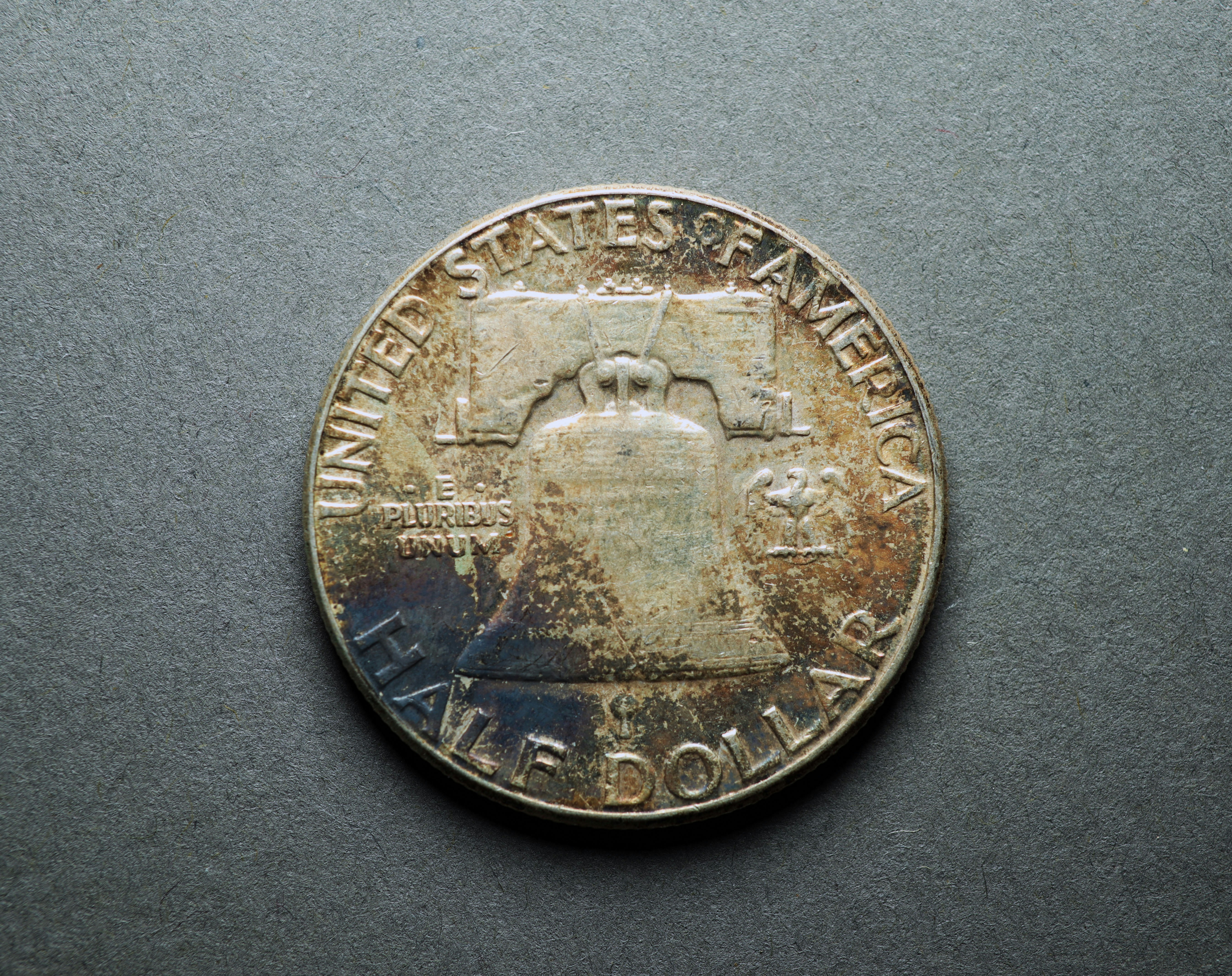 A tarnished United States half dollar coin featuring the Liberty Bell on a grey surface