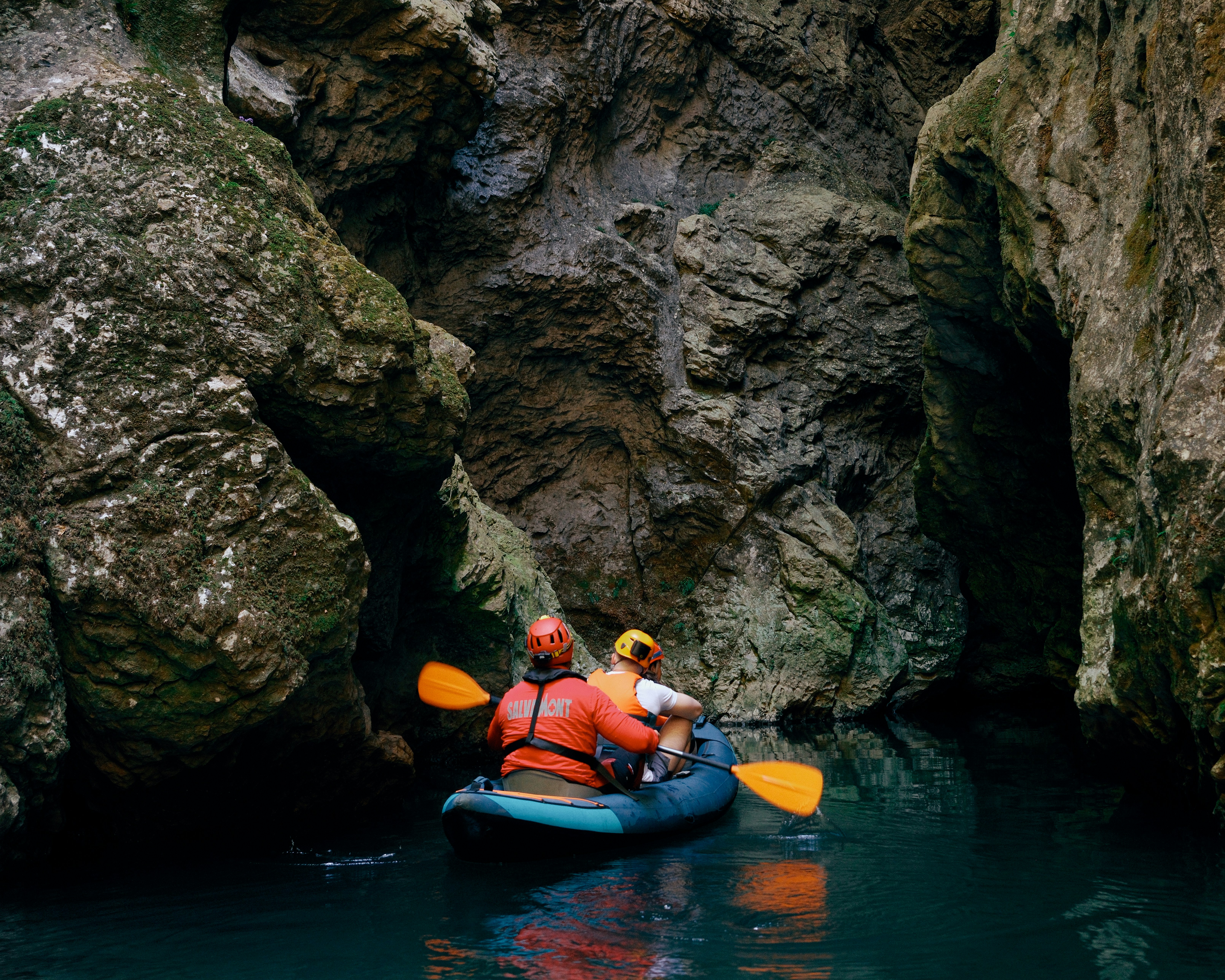 Two people in helmets and life jackets kayaking through a narrow rocky canyon