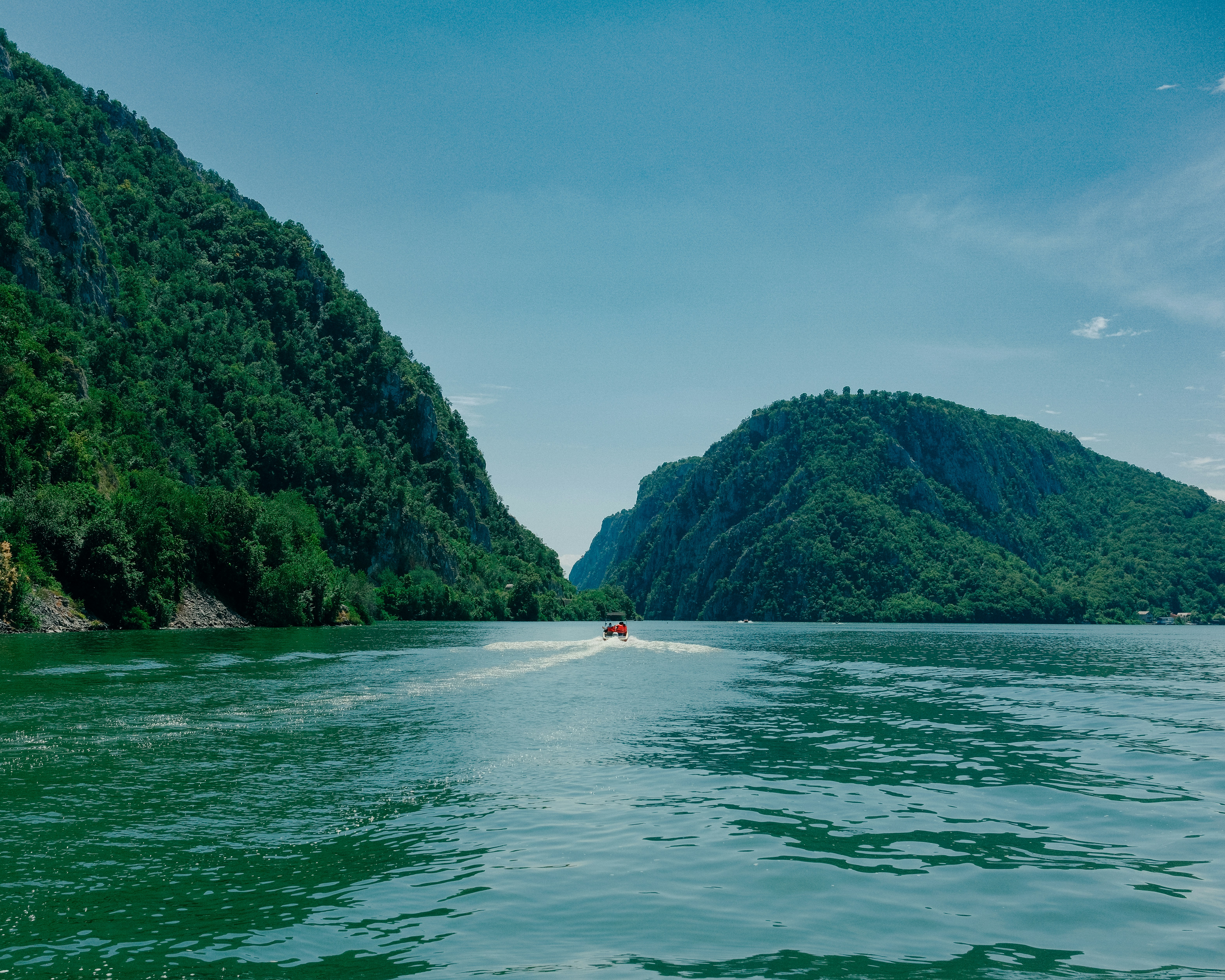 A motorboat traveling on a wide green river between steep forested mountains