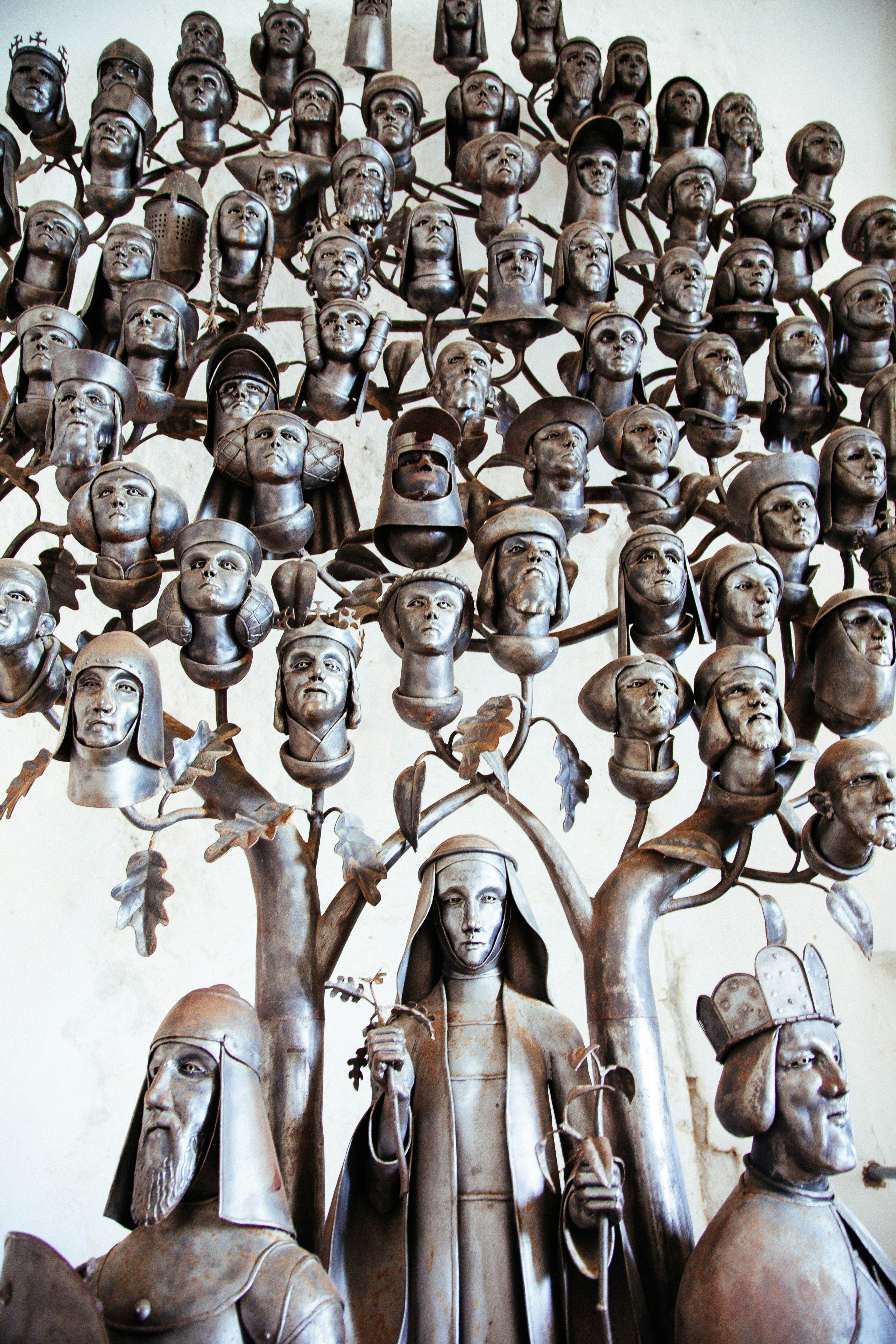 A metal sculpture of a tree with many human heads as fruit