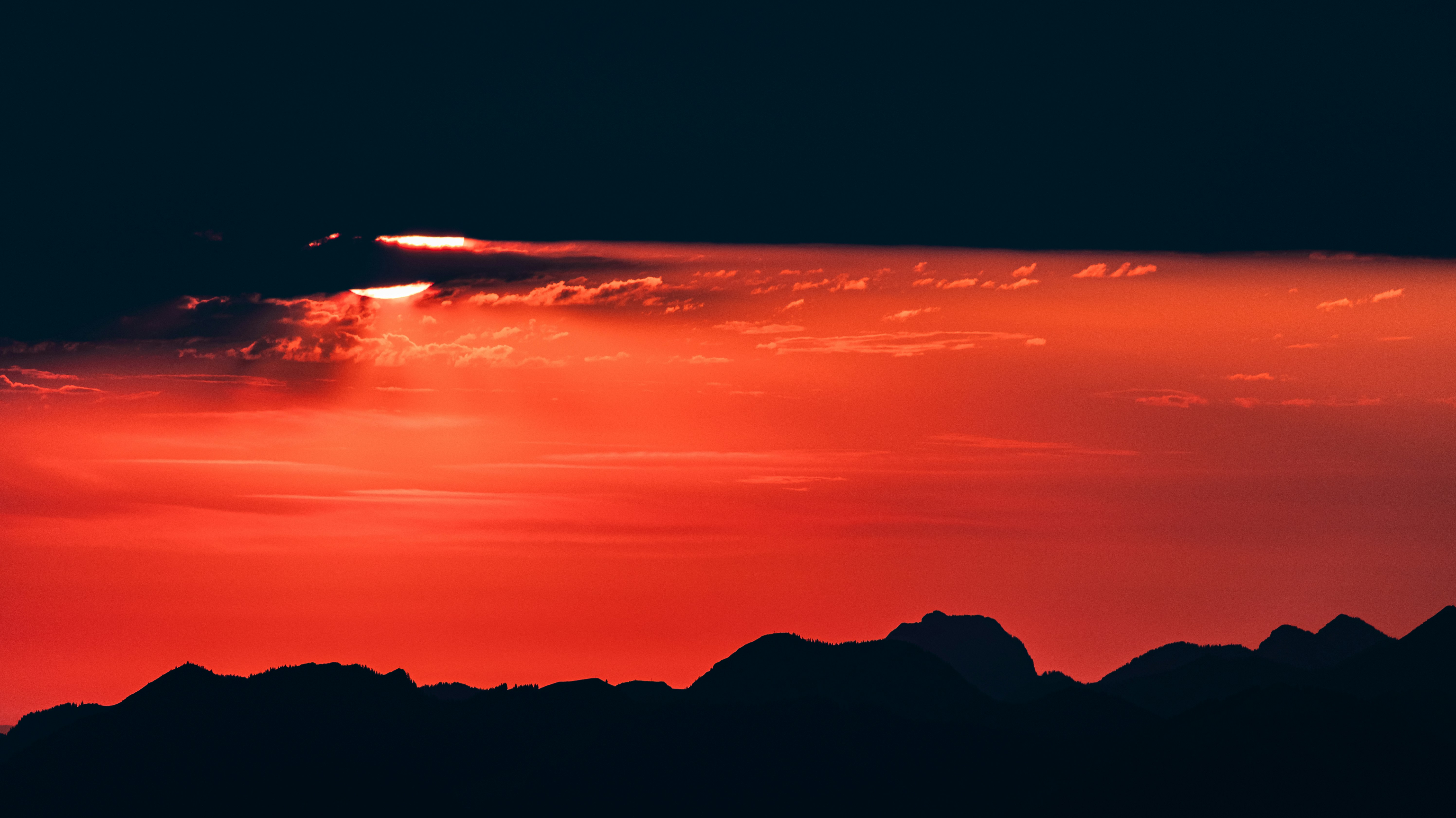 Low sun behind a dark cloud over a silhouette of mountain peaks