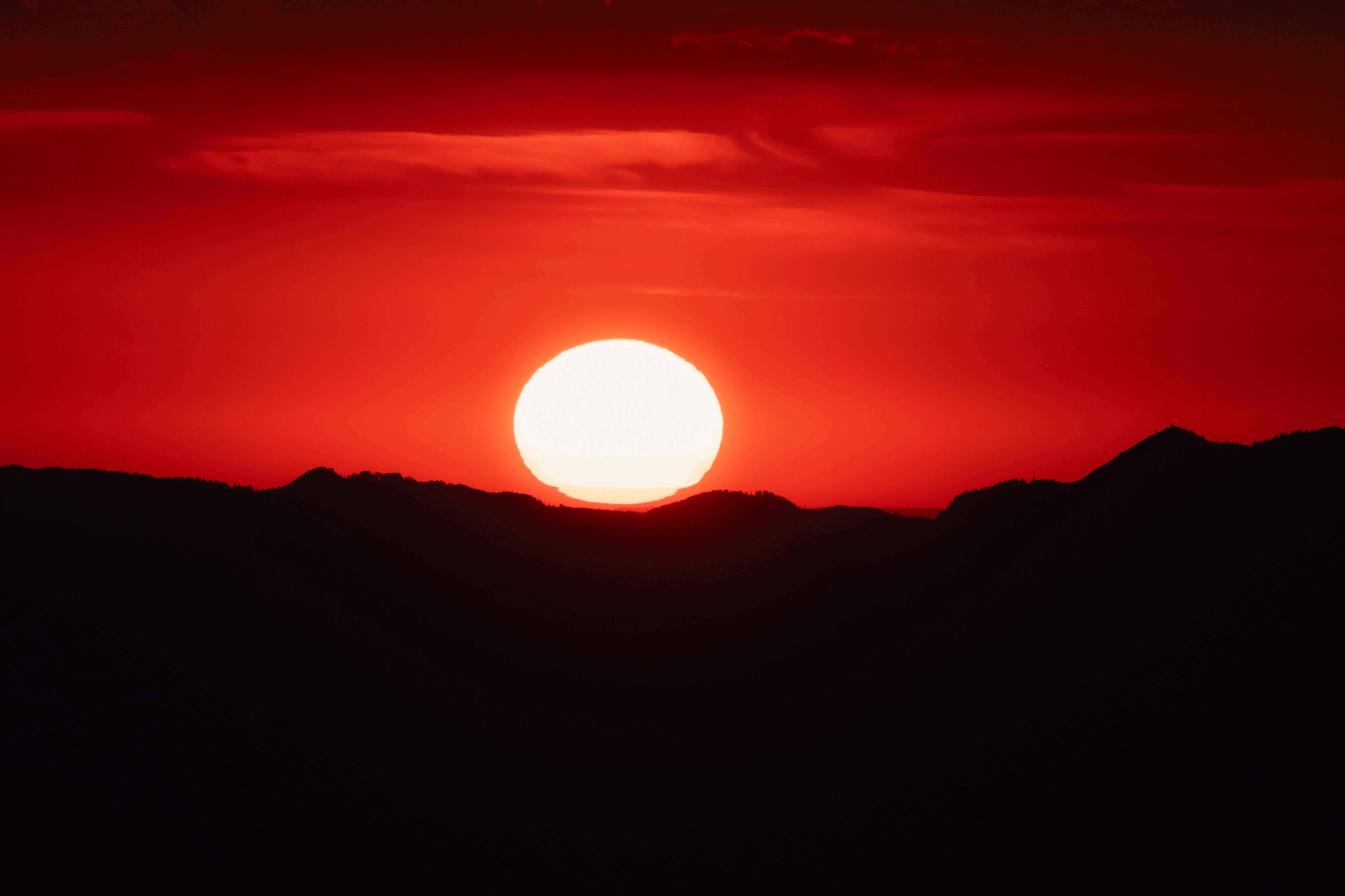 A bright low sun above a dark mountain silhouette against a red sky