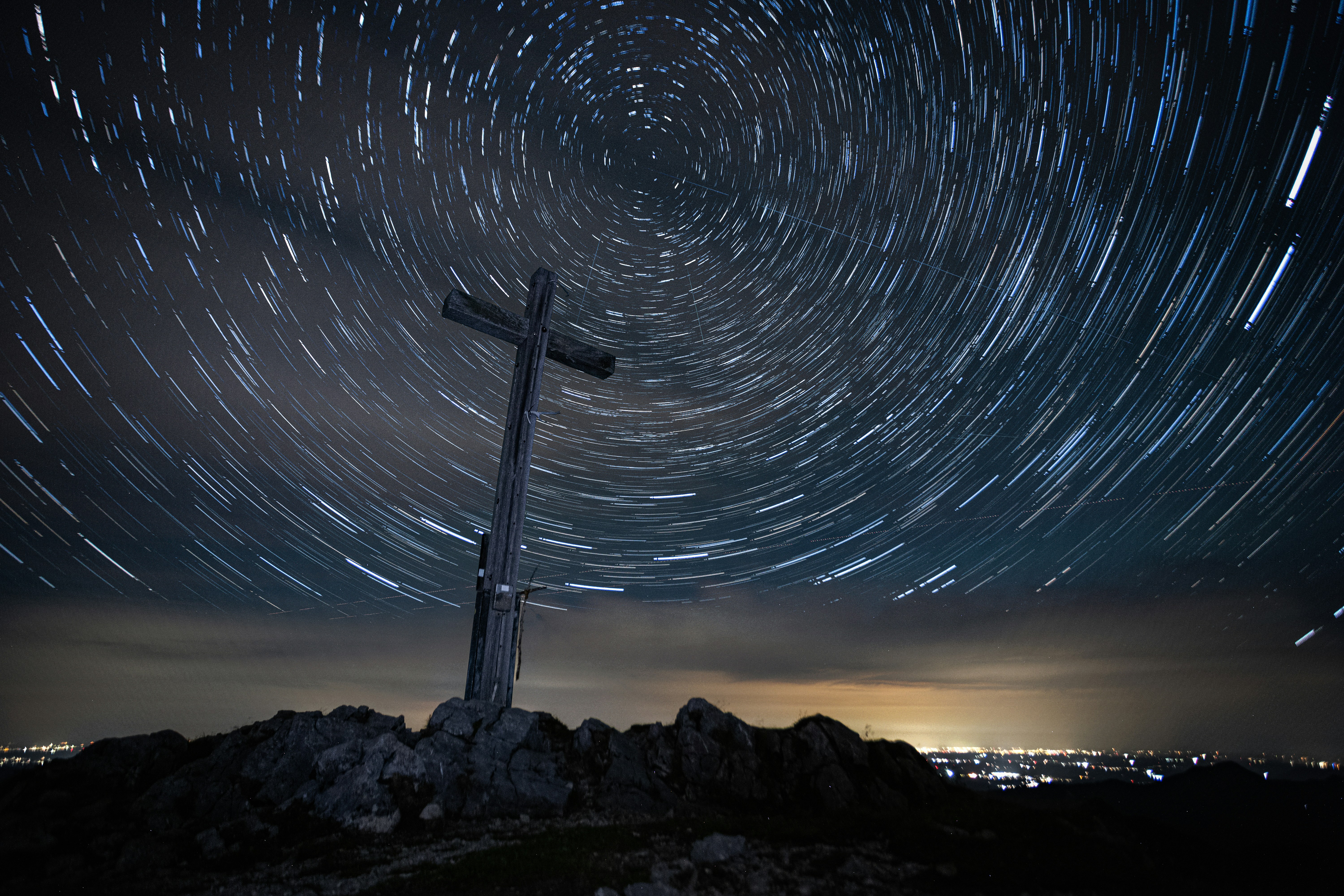 A wooden cross on a rocky summit under long exposure star trails at night