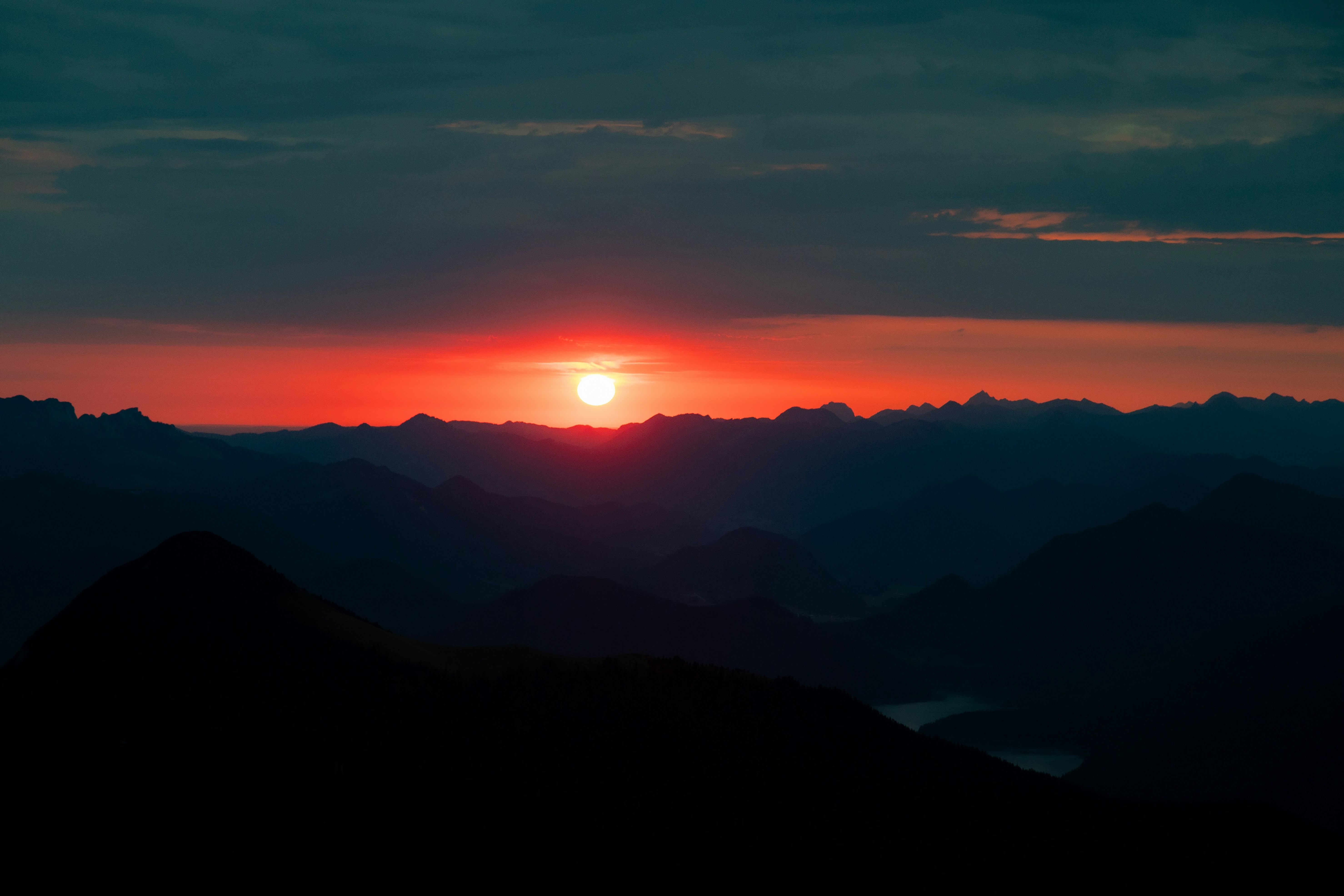 Low sun glowing red above a dark mountain range with layered silhouettes