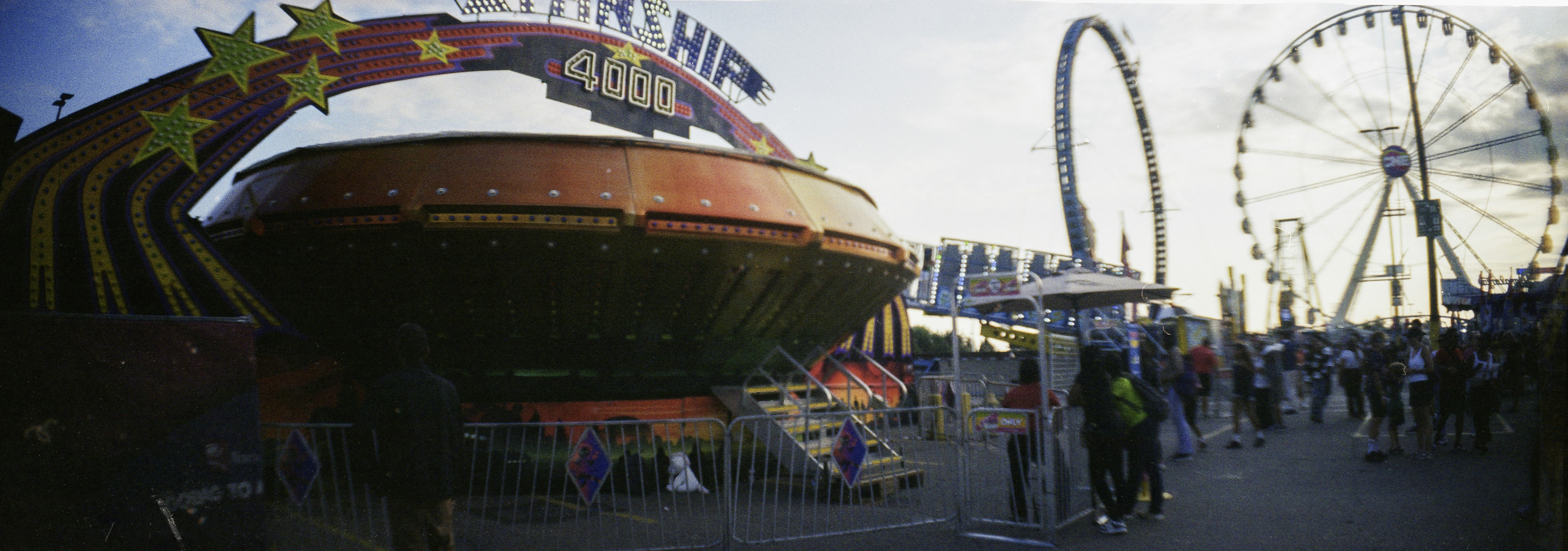A Starship 4000 carnival ride with a ferris wheel in the background at dusk