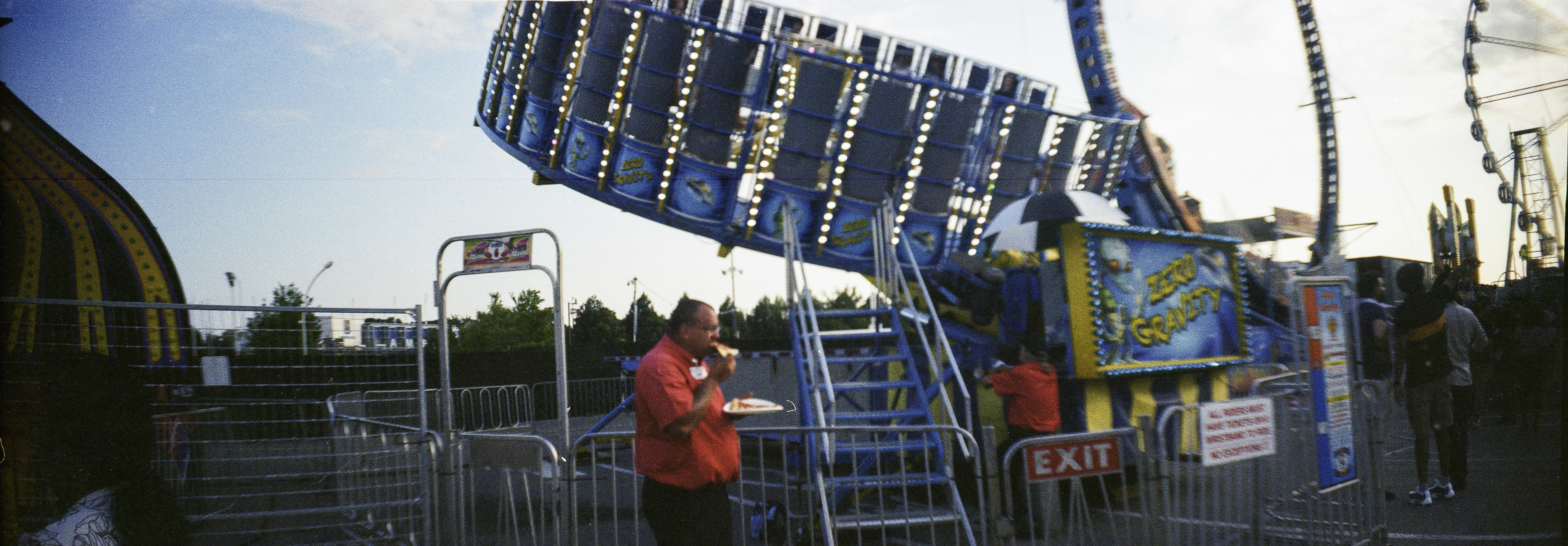 A man in a red shirt eating pizza near a carnival ride