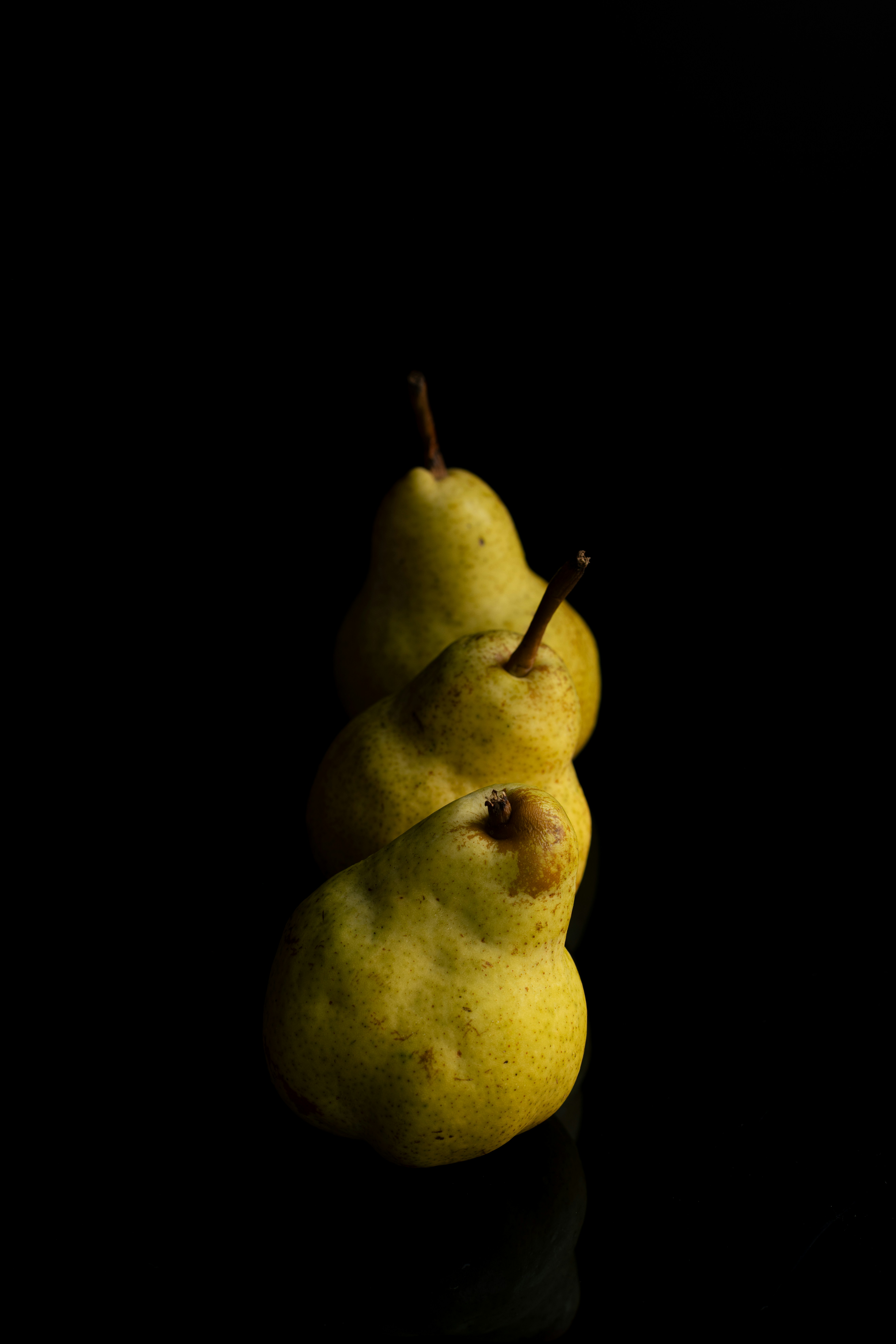 Three yellow pears in a diagonal row against a solid black background
